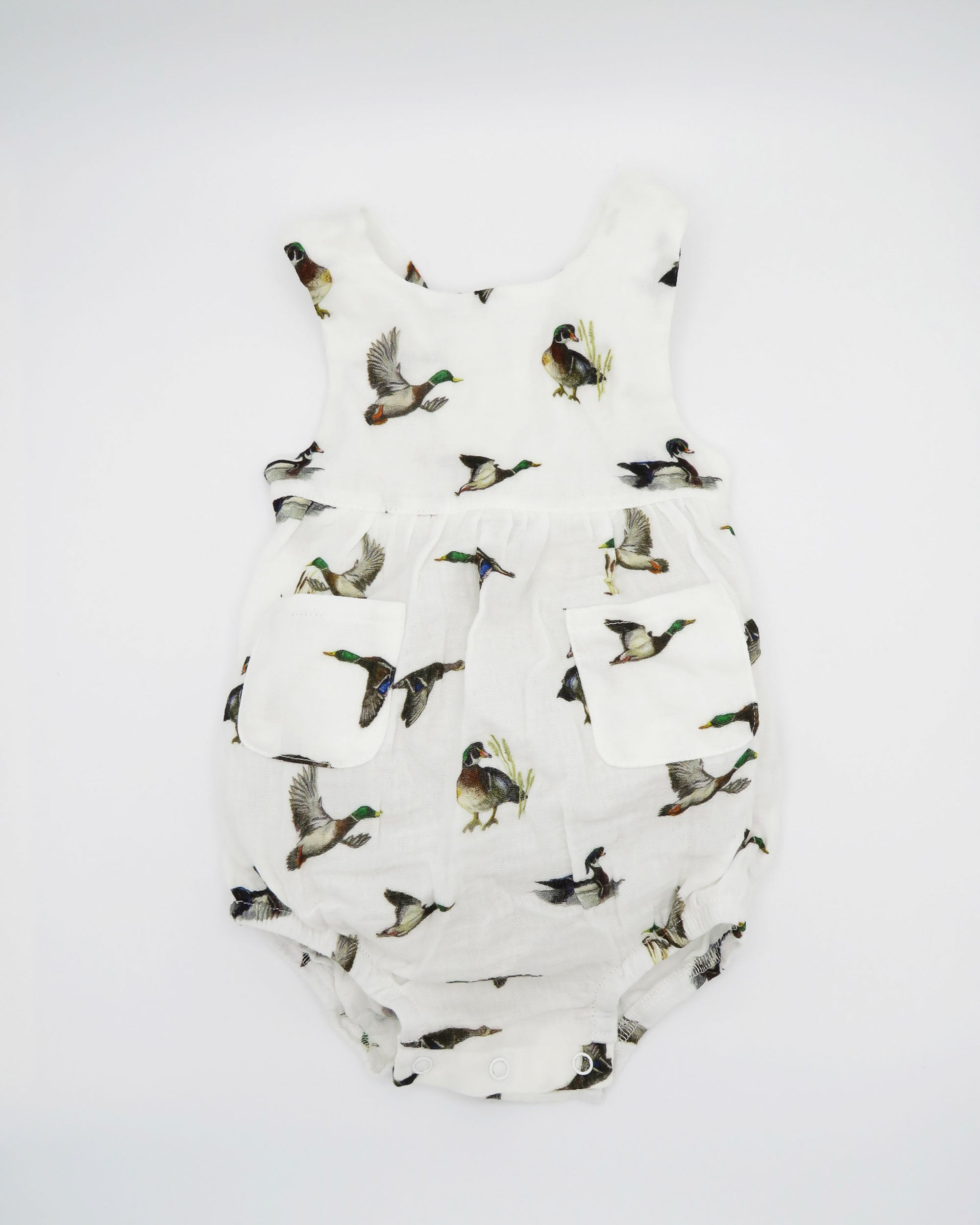 Diving ducks Best organic cotton sunsuit for kids in vibrant spring pattern. Diving Ducks printed on soft white fabric, worn by a little girl outdoors.