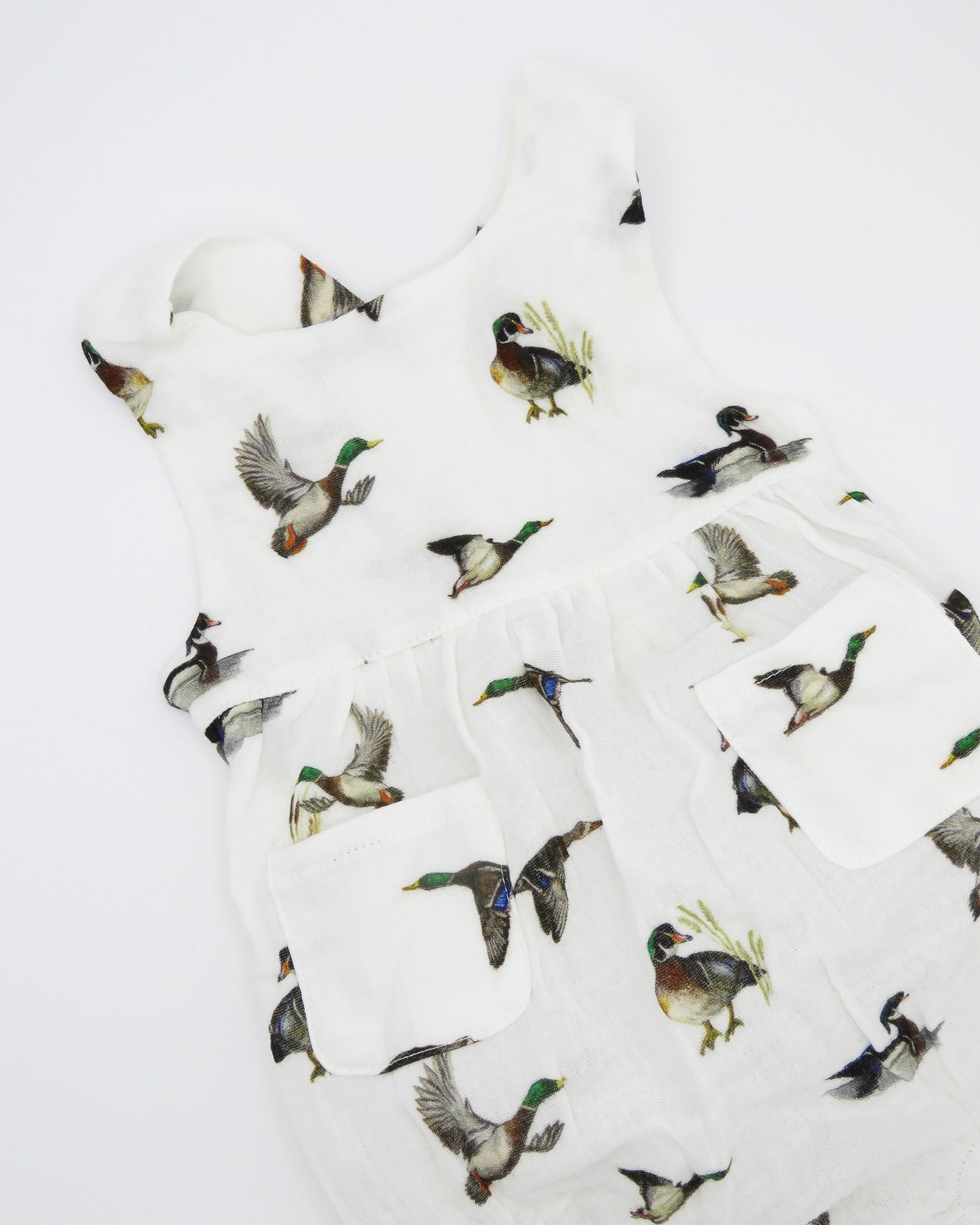Diving ducks Best organic cotton sunsuit for kids in vibrant spring pattern. Diving Ducks printed on soft white fabric, worn by a little girl outdoors.