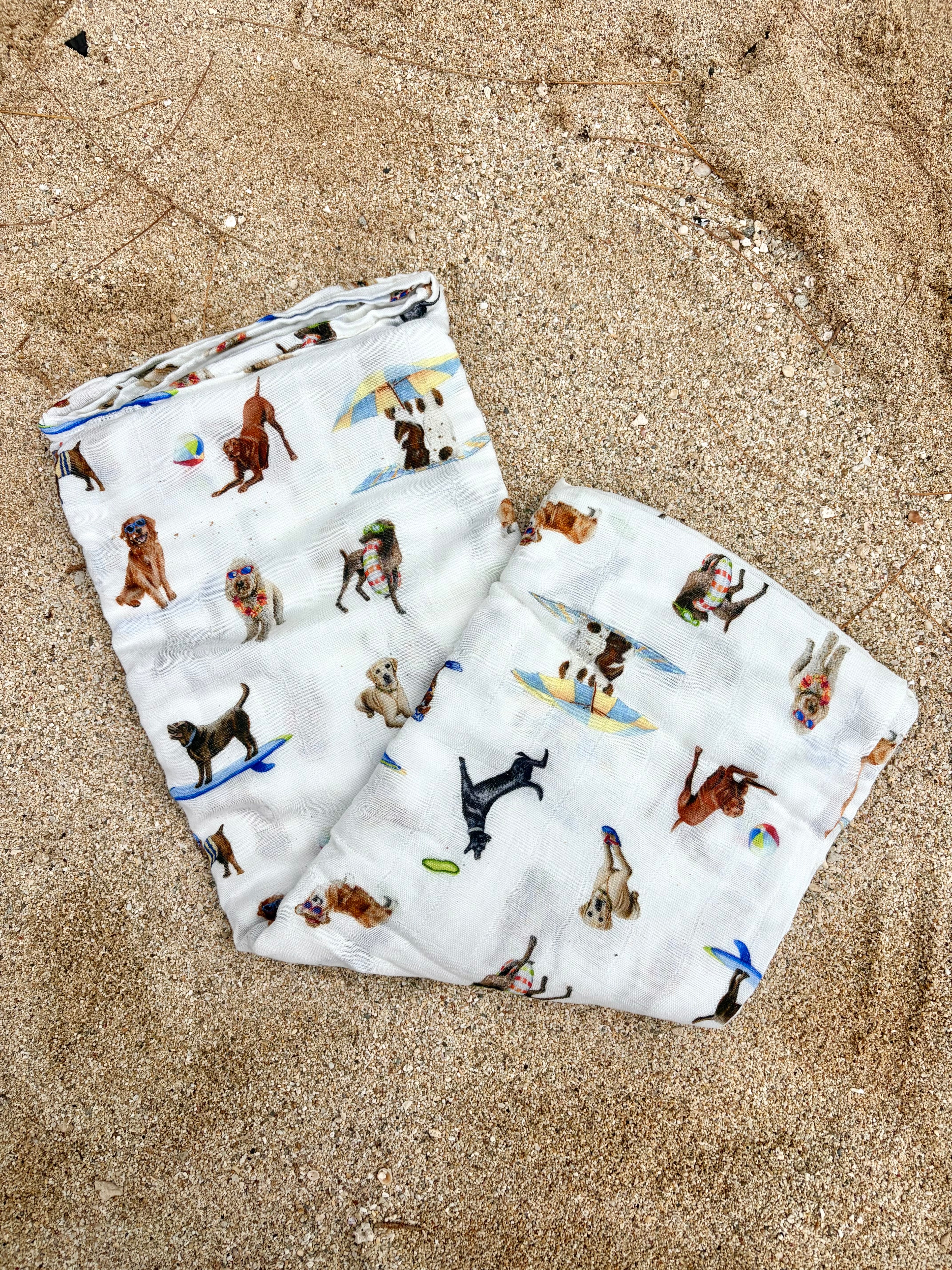 Dog Days of Summer pattern swaddle displayed folded and flat on beach sand.