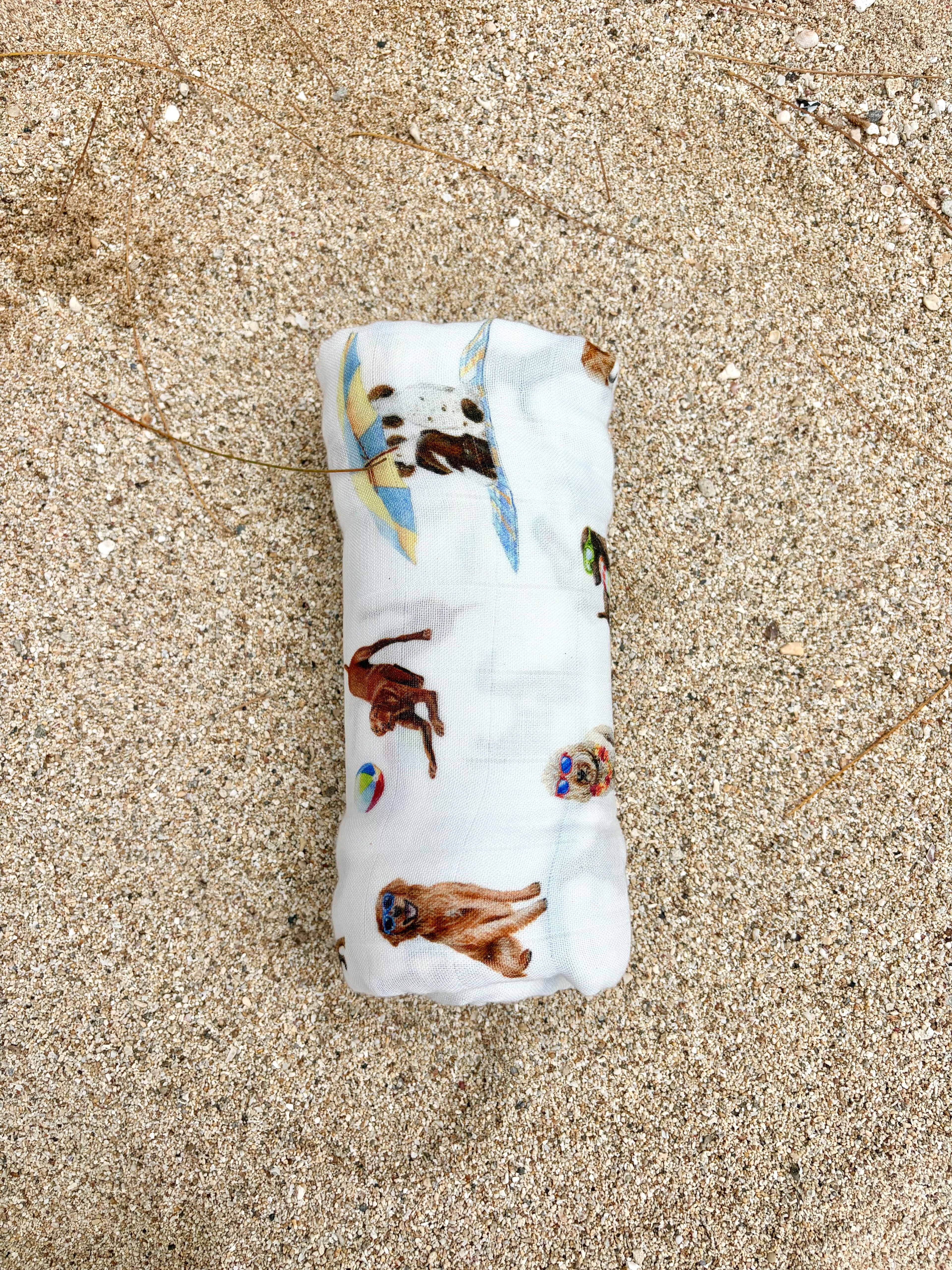 Dog Days of Summer pattern swaddle displayed rolled on beach sand.