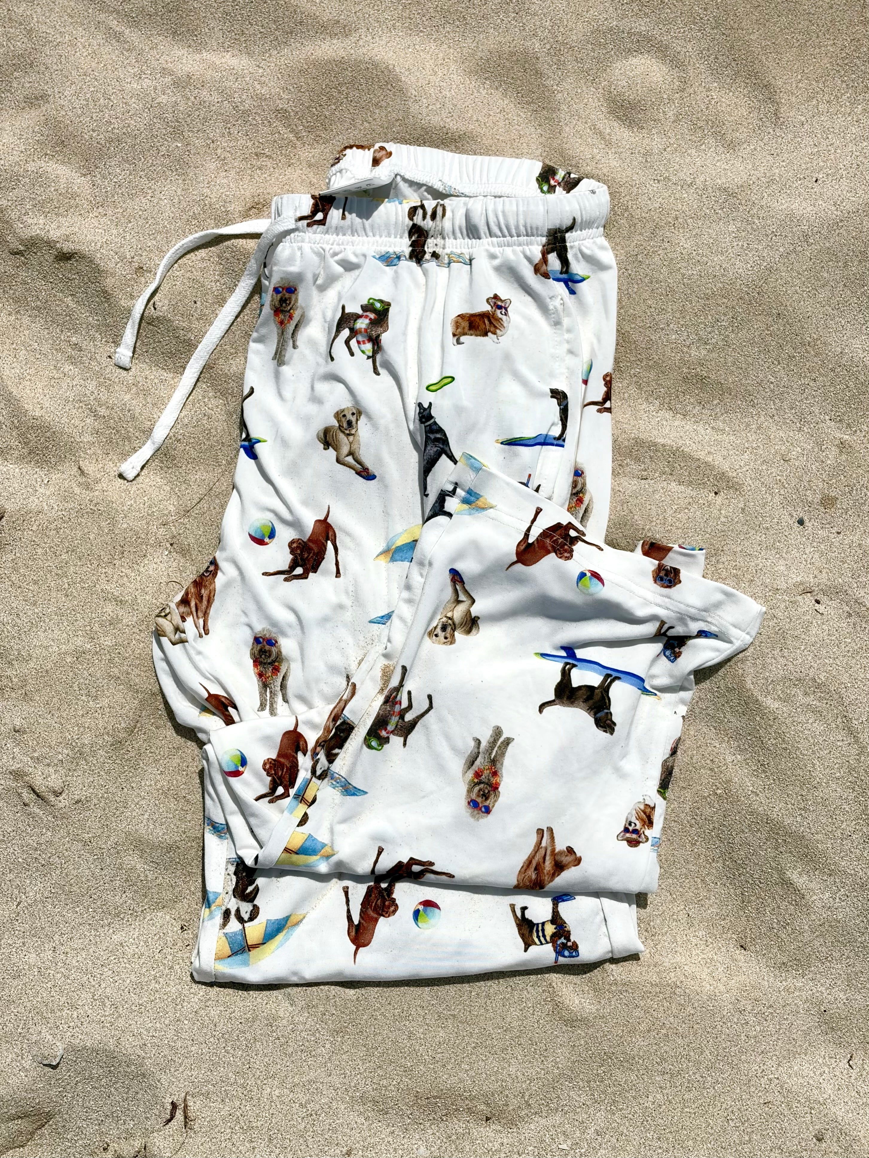 Dog Days of Summer adult pajama pants displayed folded and flat on the beach sand.