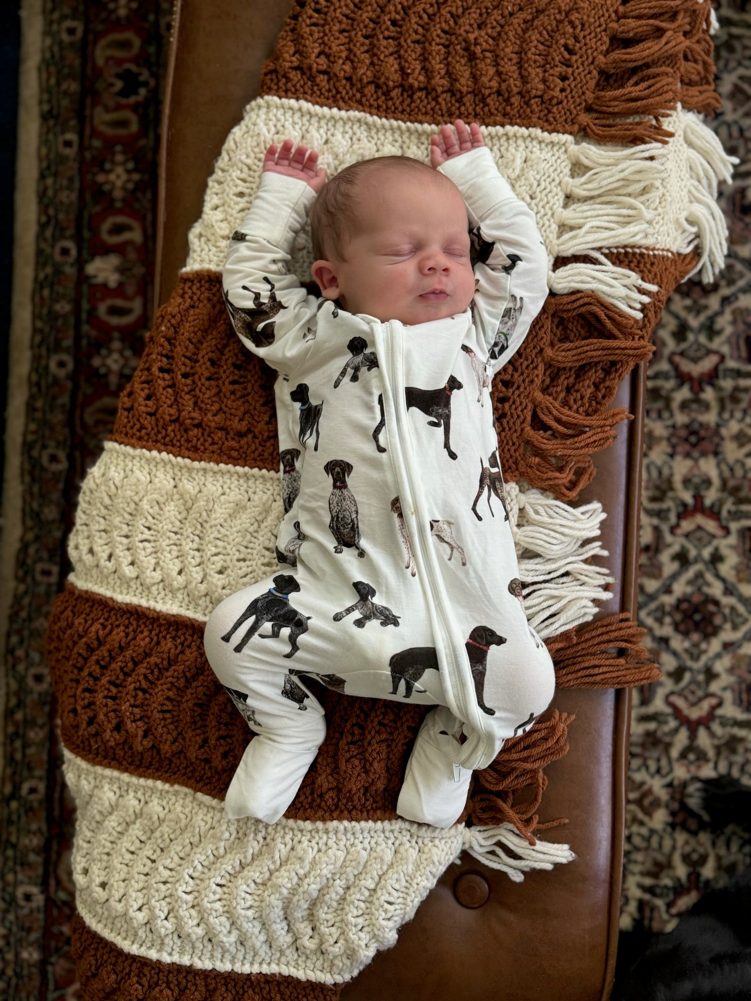 A baby lying, wearing a bamboo zip footie with a pattern of German Shorthaired Pointers.