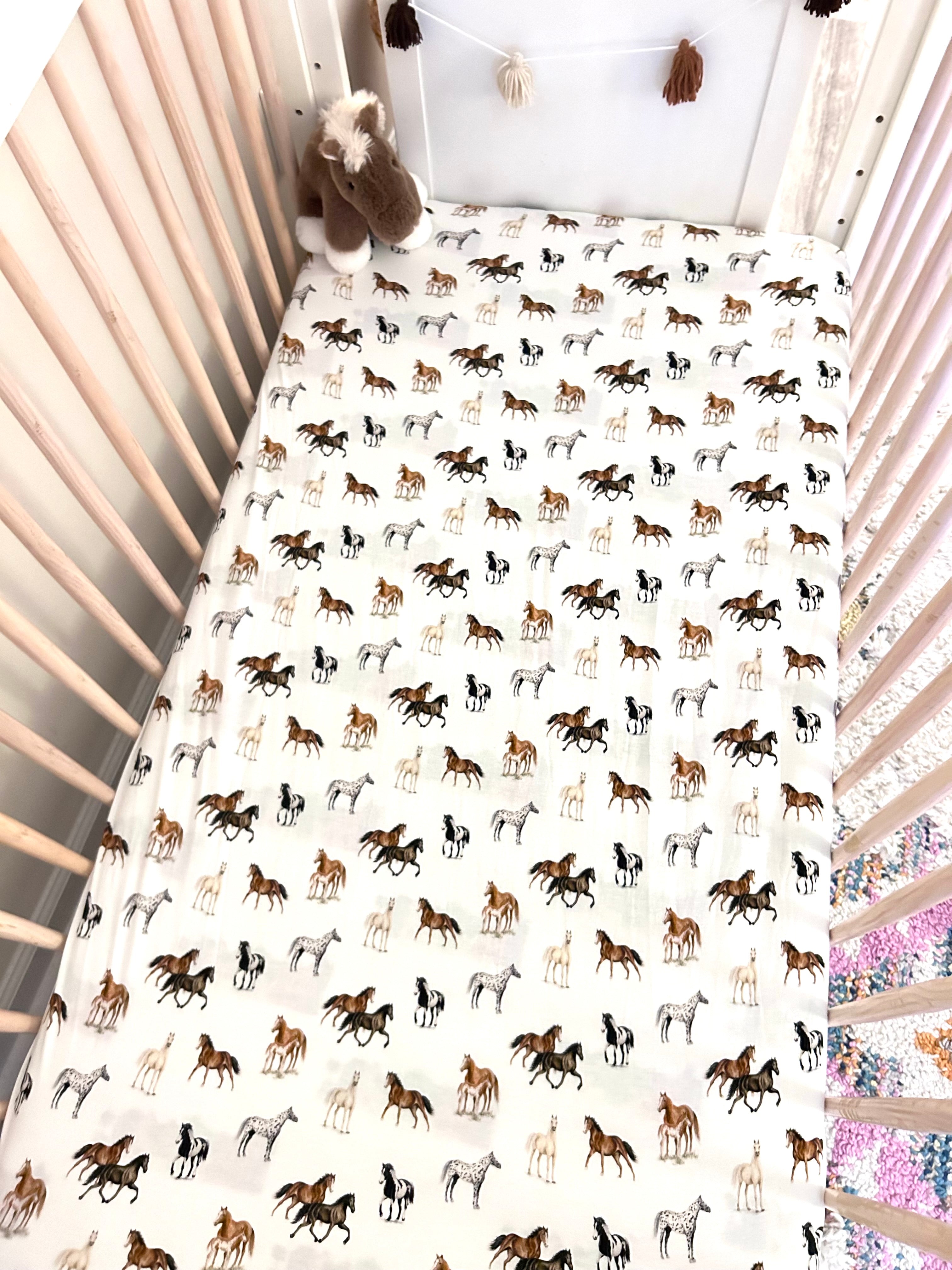 Our Harbor Horses crib sheet featuring hand-painted, colorful horses printed on soft white 100% cotton jersey, fitted for cribs or toddler beds, perfect for a horse-themed nursery.