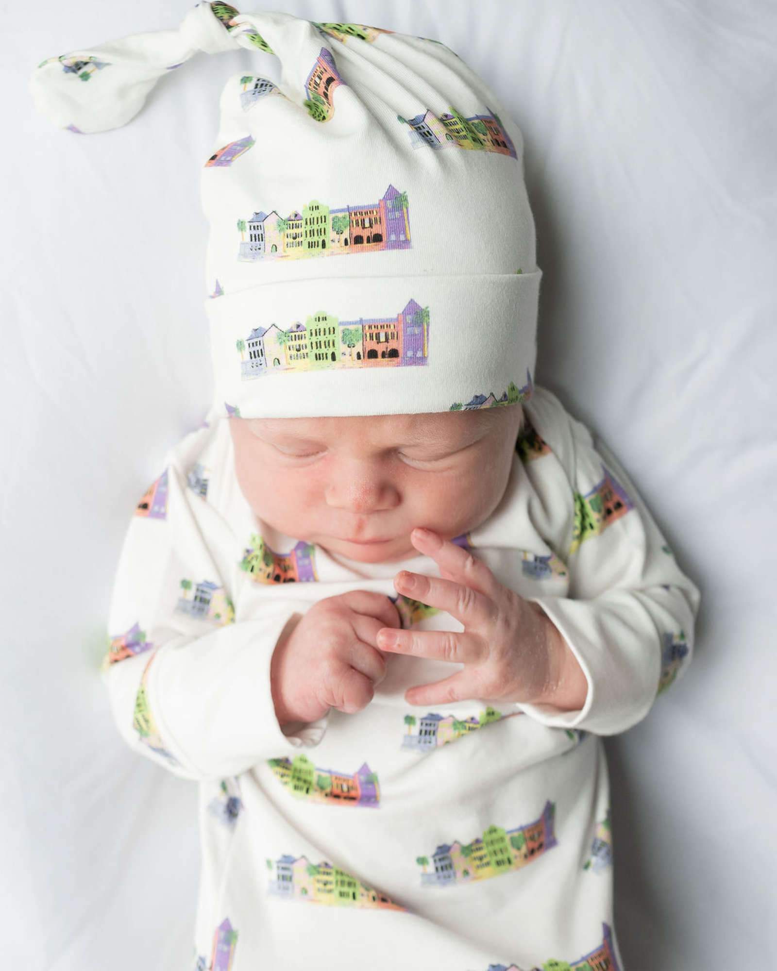 Baby wrapped in cozy Rainbow Row-themed gown and hat, capturing early memories