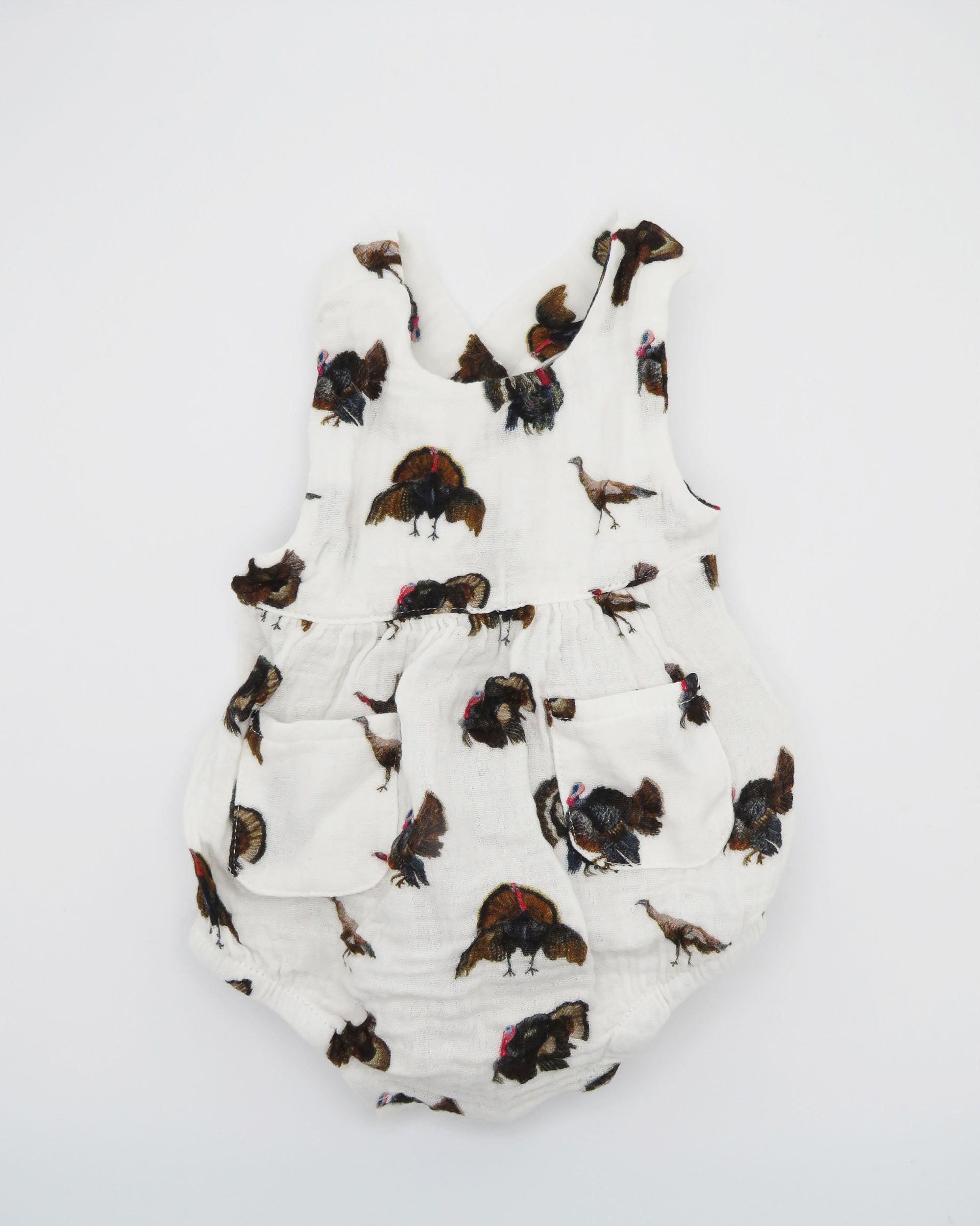 Turkey Trot baby sunsuit in soft white fabric with a playful turkey print, lightweight and comfortable for all-day wear. Perfect for keeping babies cozy indoors or outdoors, ideal for festive fall or Thanksgiving outfits. Displayed flat on white background.