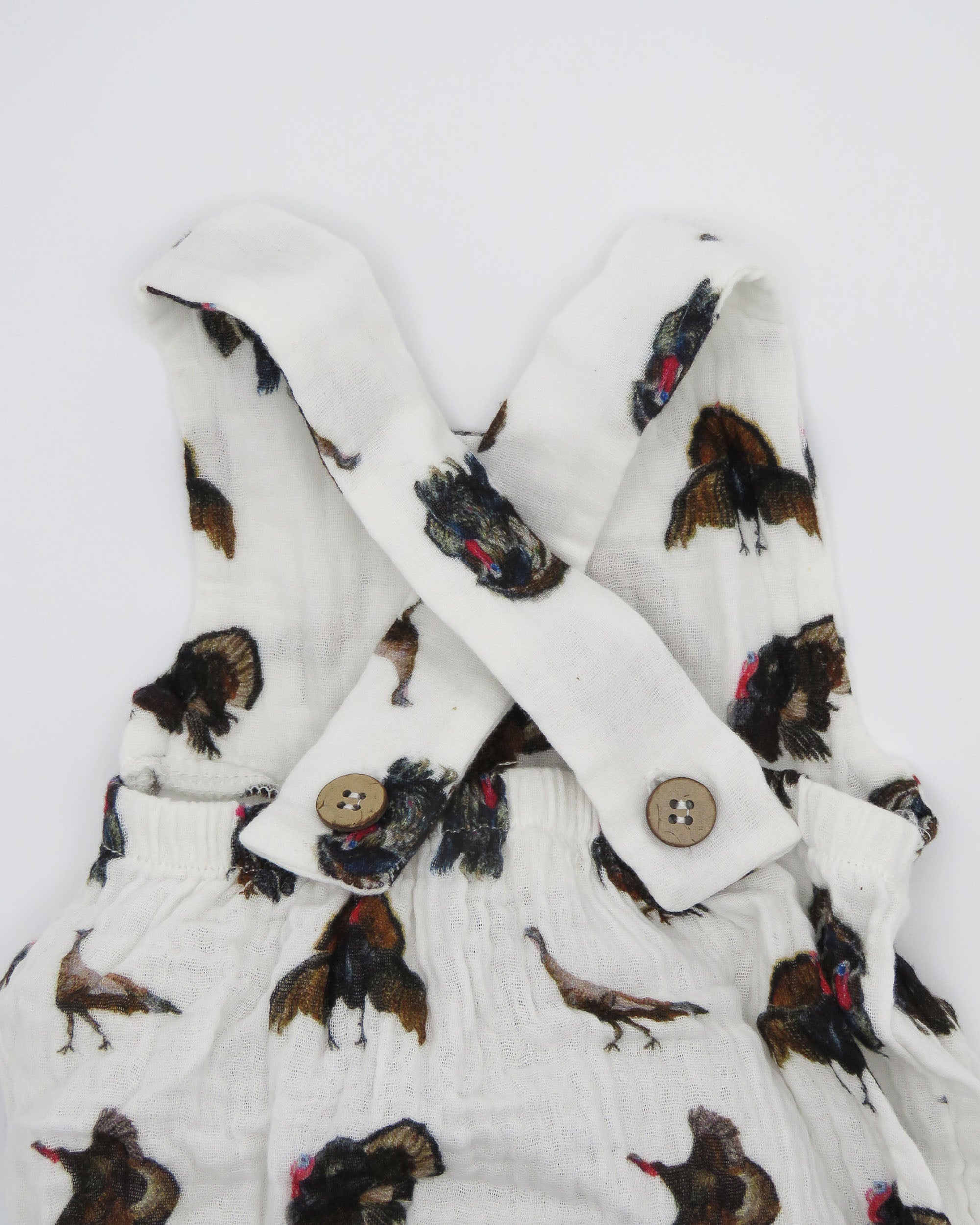 Turkey Trot baby sunsuit in soft white fabric with a playful turkey print, lightweight and comfortable for all-day wear. Perfect for keeping babies cozy indoors or outdoors, ideal for festive fall or Thanksgiving outfits. Displayed flat on white background.
