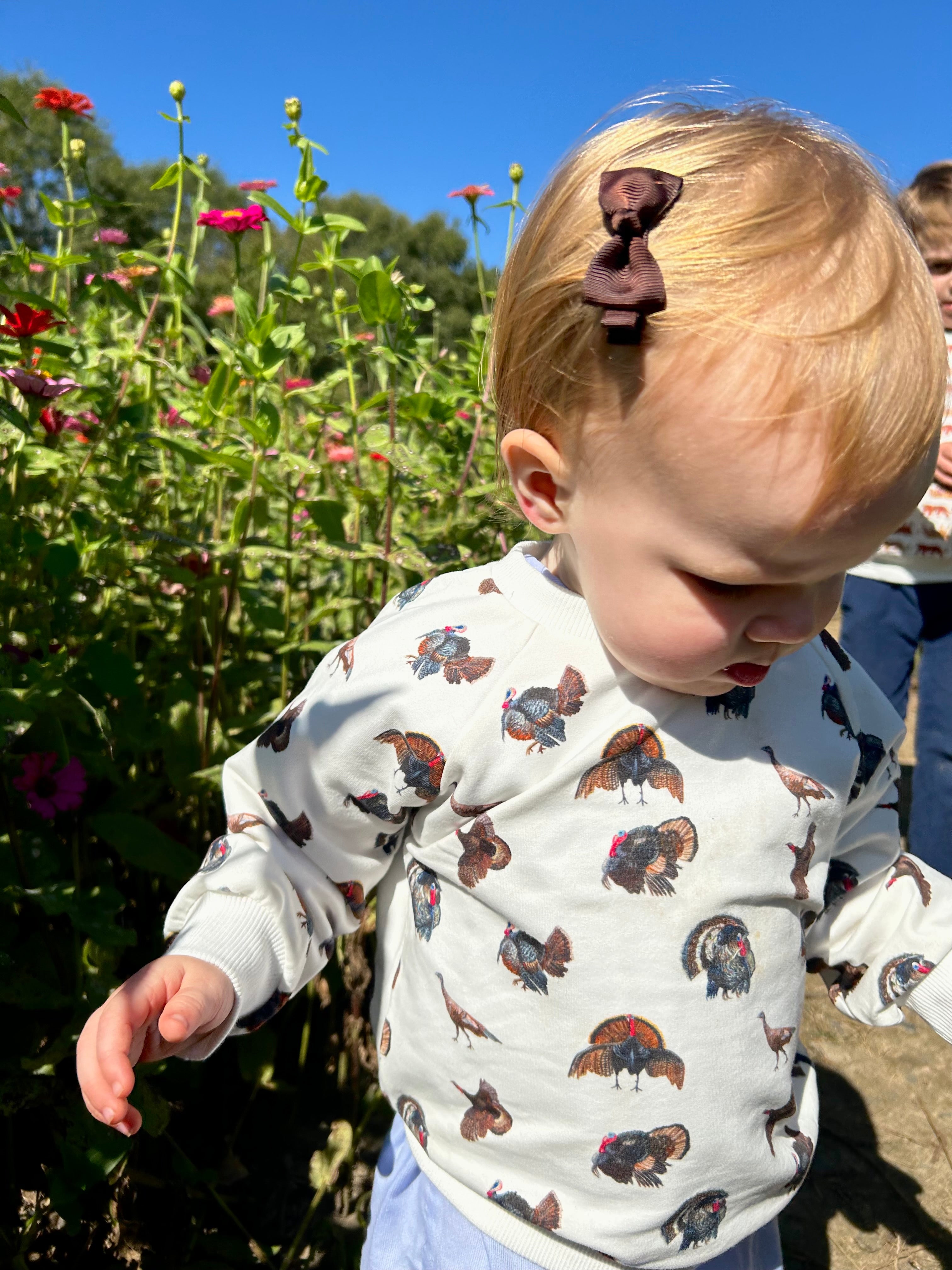 Turkey Trot kids’ drop sleeve sweatshirt in soft white fabric with a playful turkey print, cozy and comfortable for indoors or outdoors. Shown worn by a little girl playing outside.