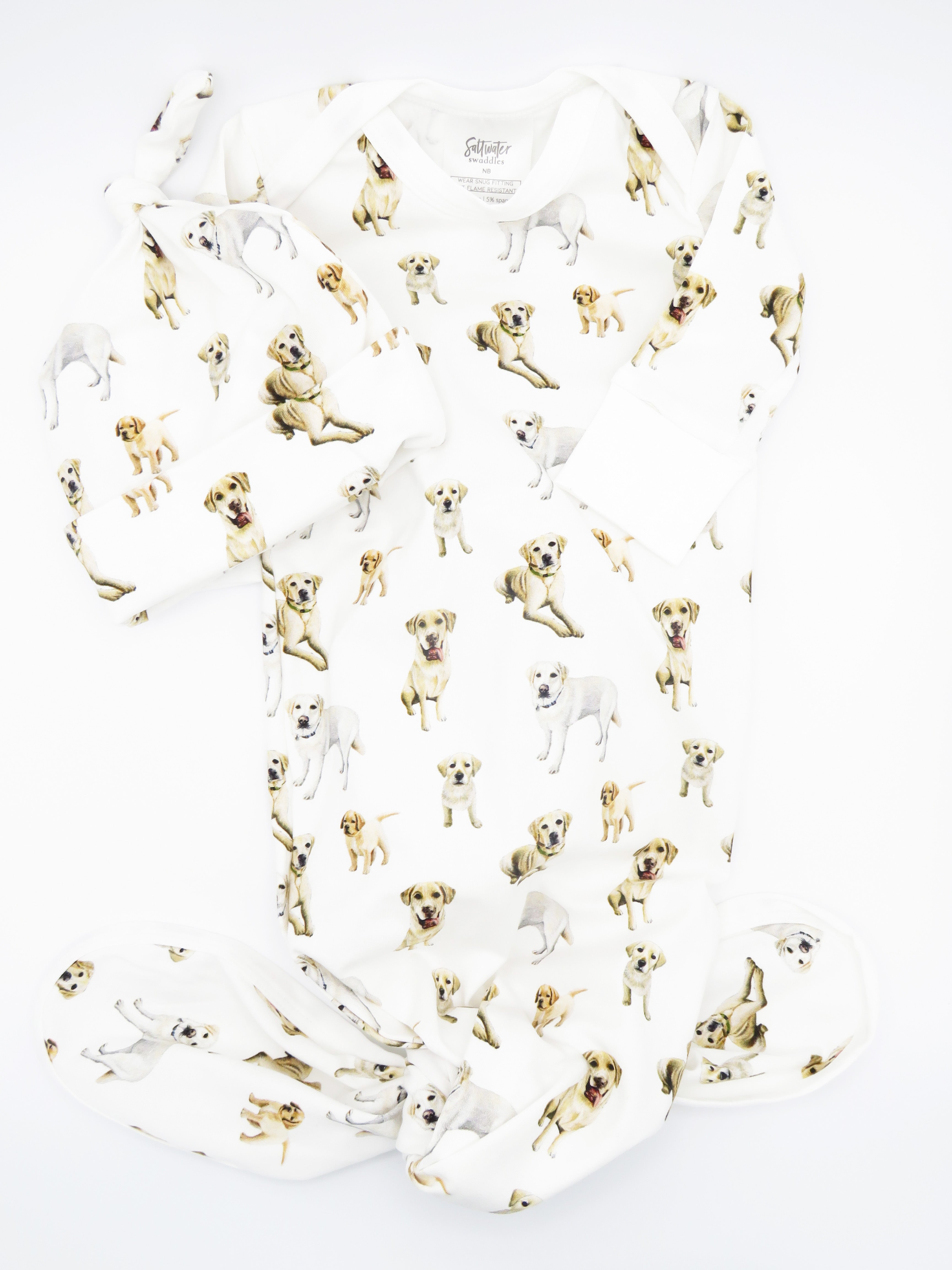 Newborn baby wearing a Yellow Labrador–printed outfit and hat on soft white fabric.