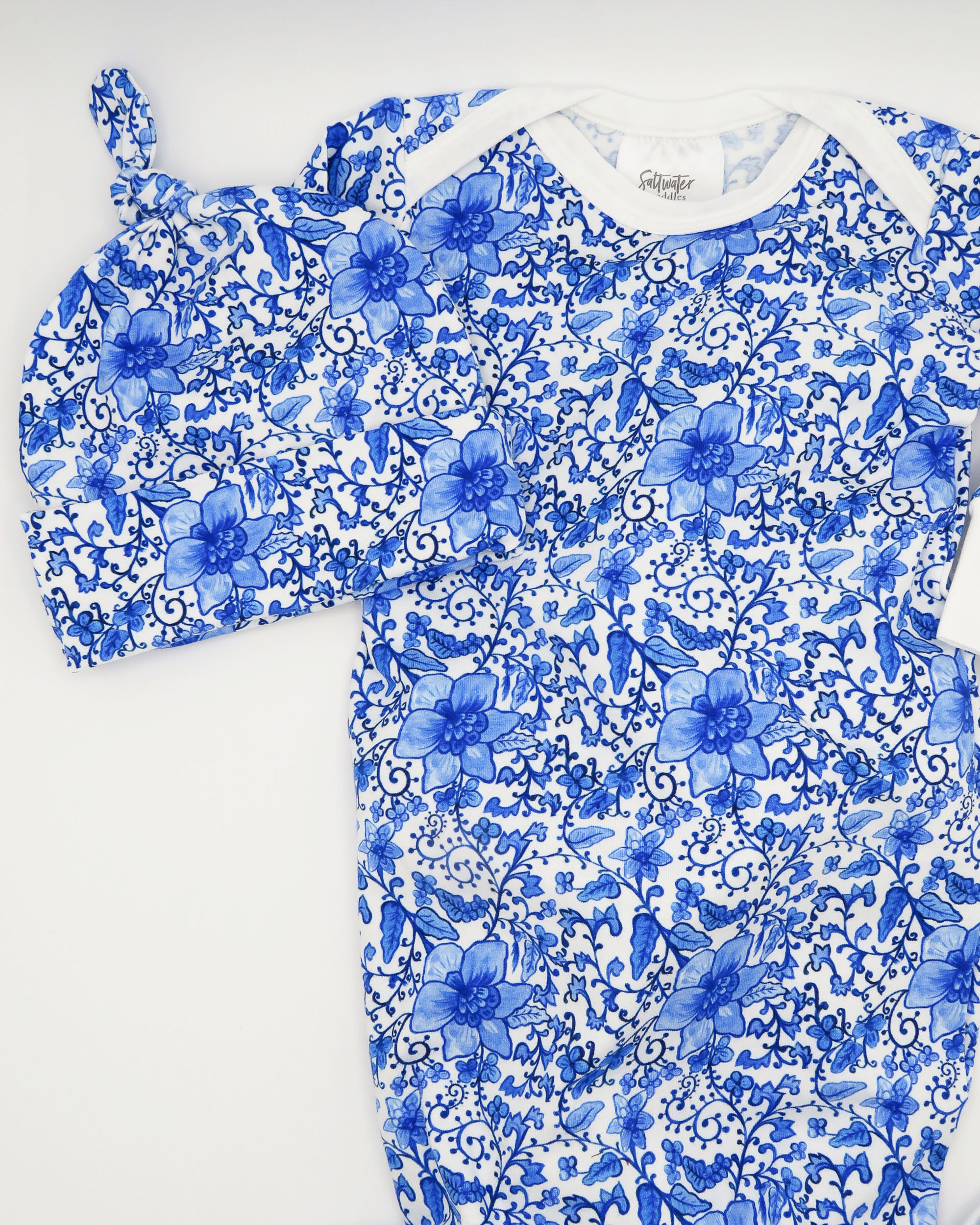 Charming newborn gown and matching hat featuring a timeless Chinoiserie print on soft white fabric, perfect for special newborn moments. Displayed on a white background.