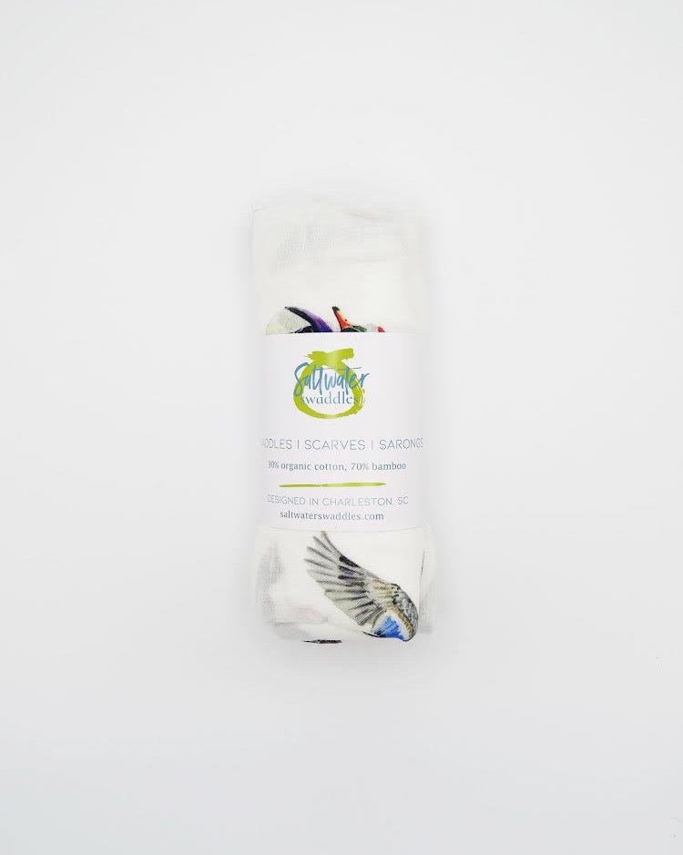 A swaddled baby with a white hat on, wrapped in a blanket with a printed design featuring christmas ducks.