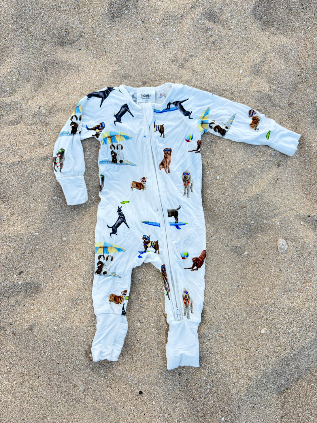 Beach Dogs pattern Convertible Zip Footies, made from 100% bamboo and printed on soft white fabric. Displayed flat on the beach sand.