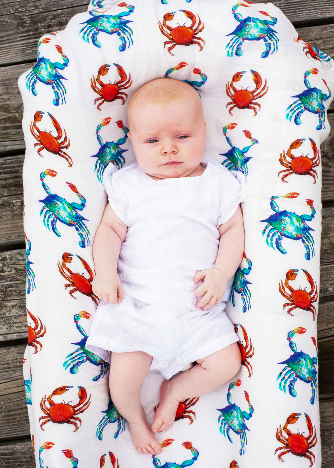 A newborn swaddled in a blanket with vibrant hand-painted crab patterns.