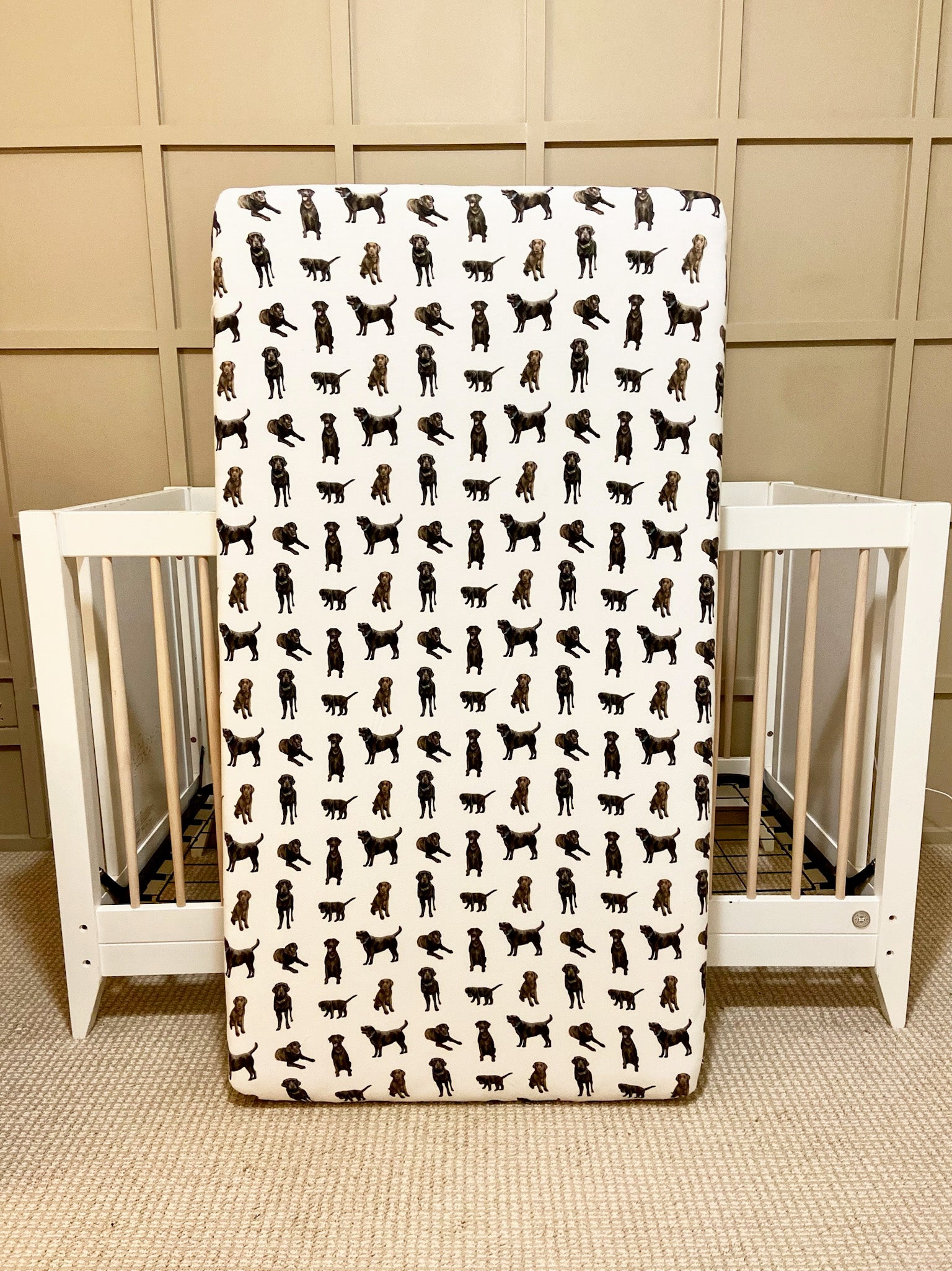 A crib sheet with a pattern of chocolate labs, displayed in front of a crib.
