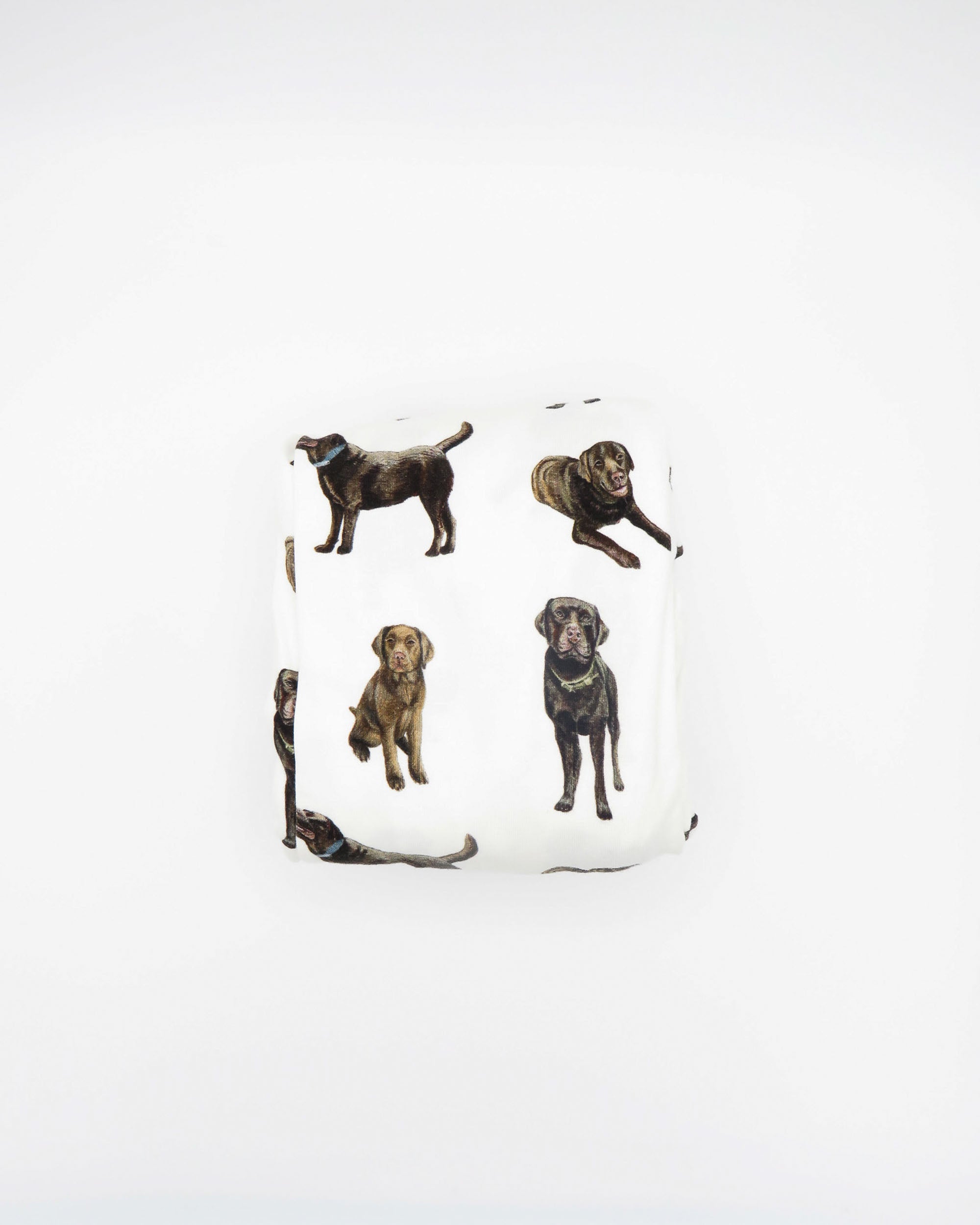 A white crib sheet with a chocolate labrador retriever print, displayed and folded on a white background.