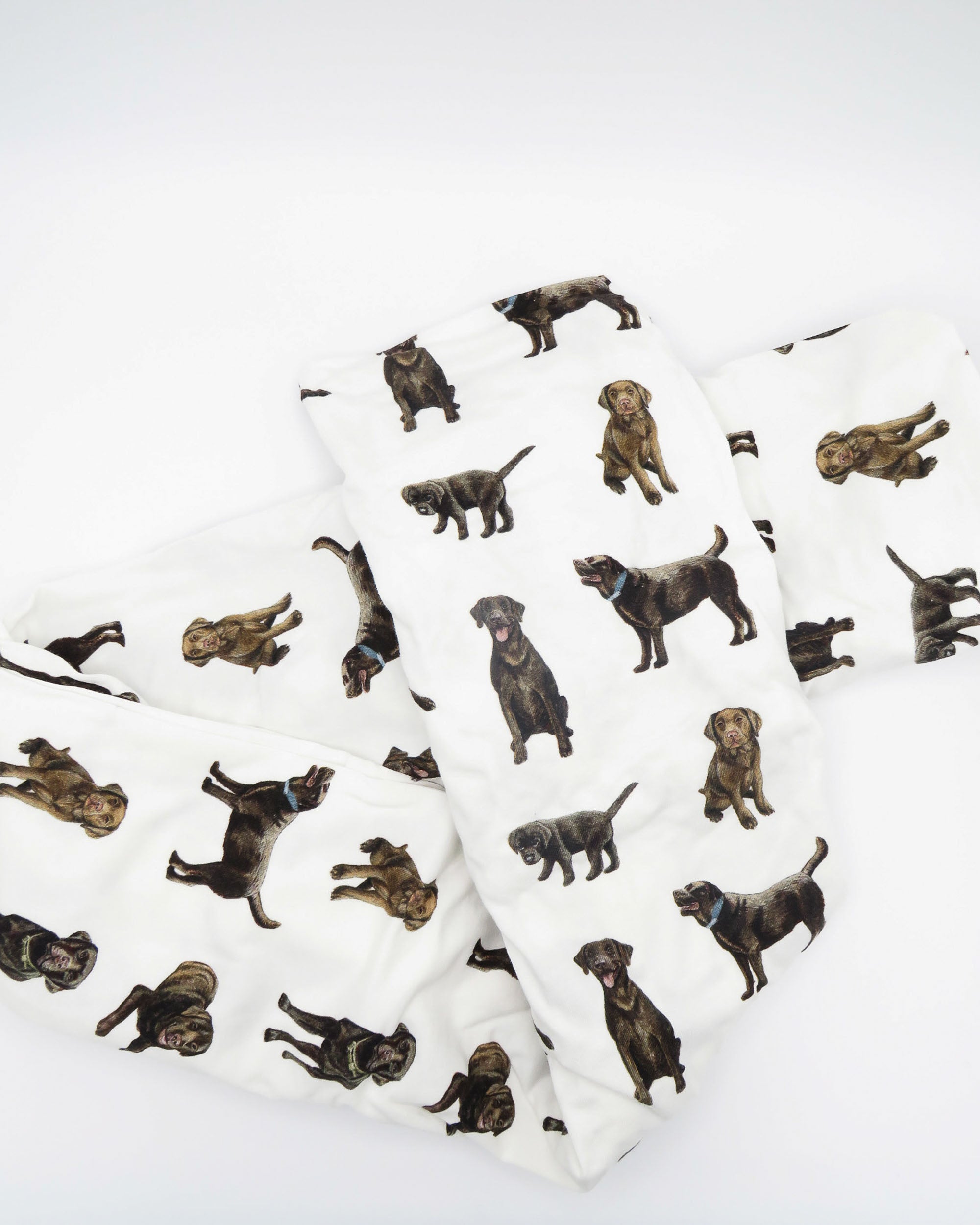 A white crib sheet with a chocolate labrador retriever print, displayed and folded on a white background.