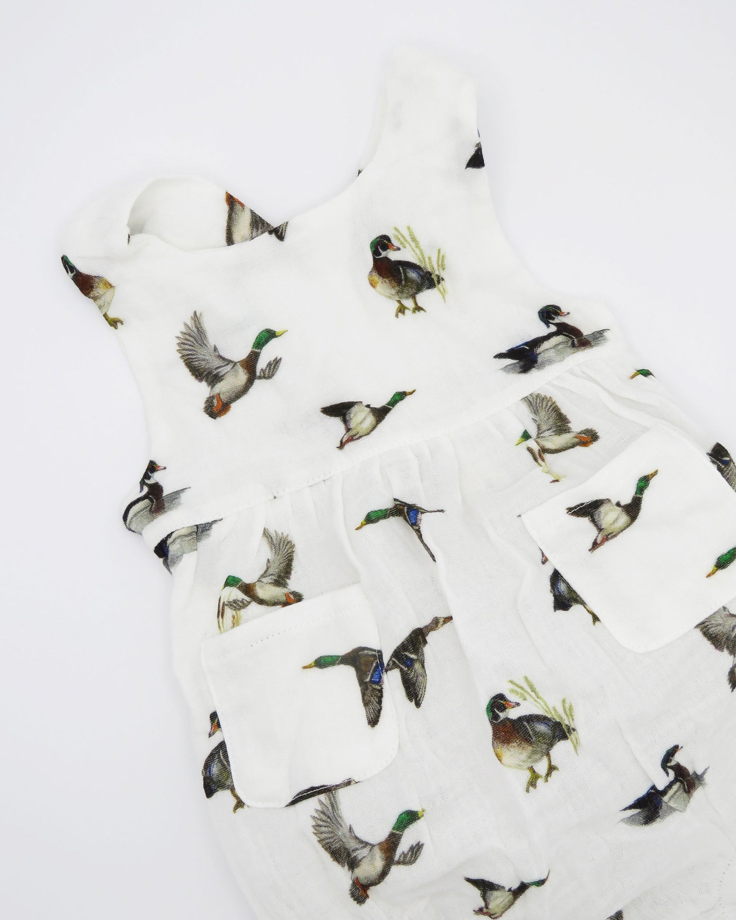 Diving ducks Best organic cotton sunsuit for kids in vibrant spring pattern. Diving Ducks printed on soft white fabric, worn by a little girl outdoors.