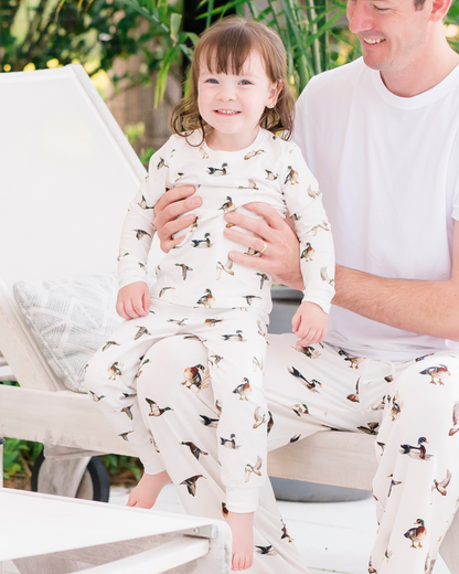 Unisex loungewear or sleepwear featuring a Diving Ducks print on soft white fabric. Kids’ pajamas worn by a little girl with her dad in matching Diving Ducks patterns. Perfect for both indoor and outdoor wear.