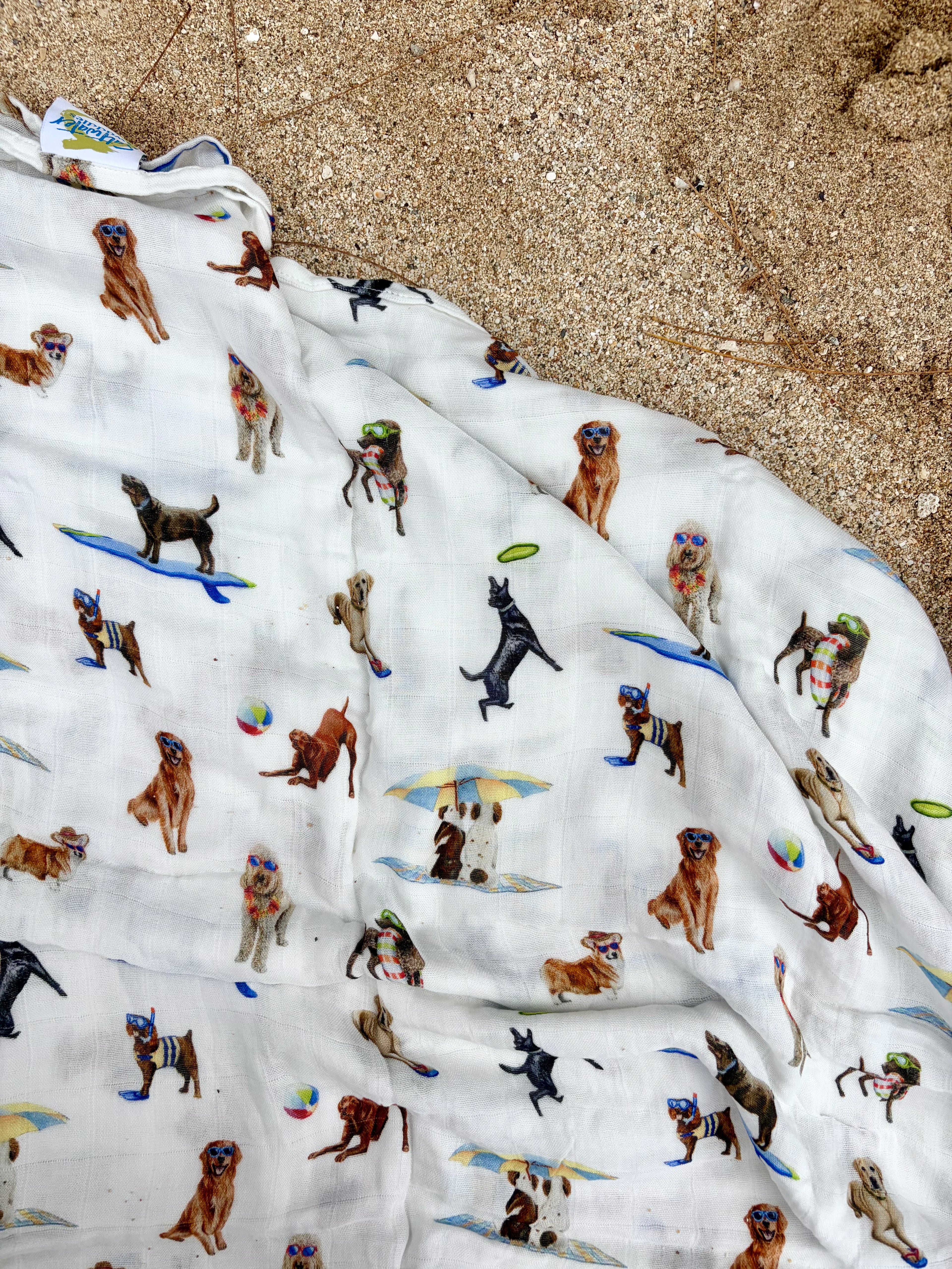 Dog Days of Summer pattern swaddle displayed on beach sand.