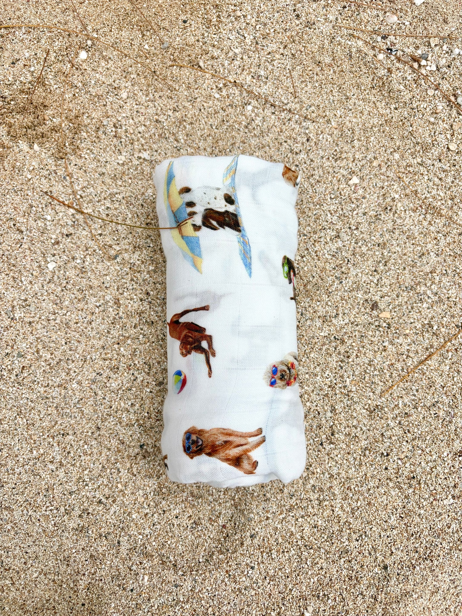 Dog Days of Summer pattern swaddle displayed rolled on beach sand.
