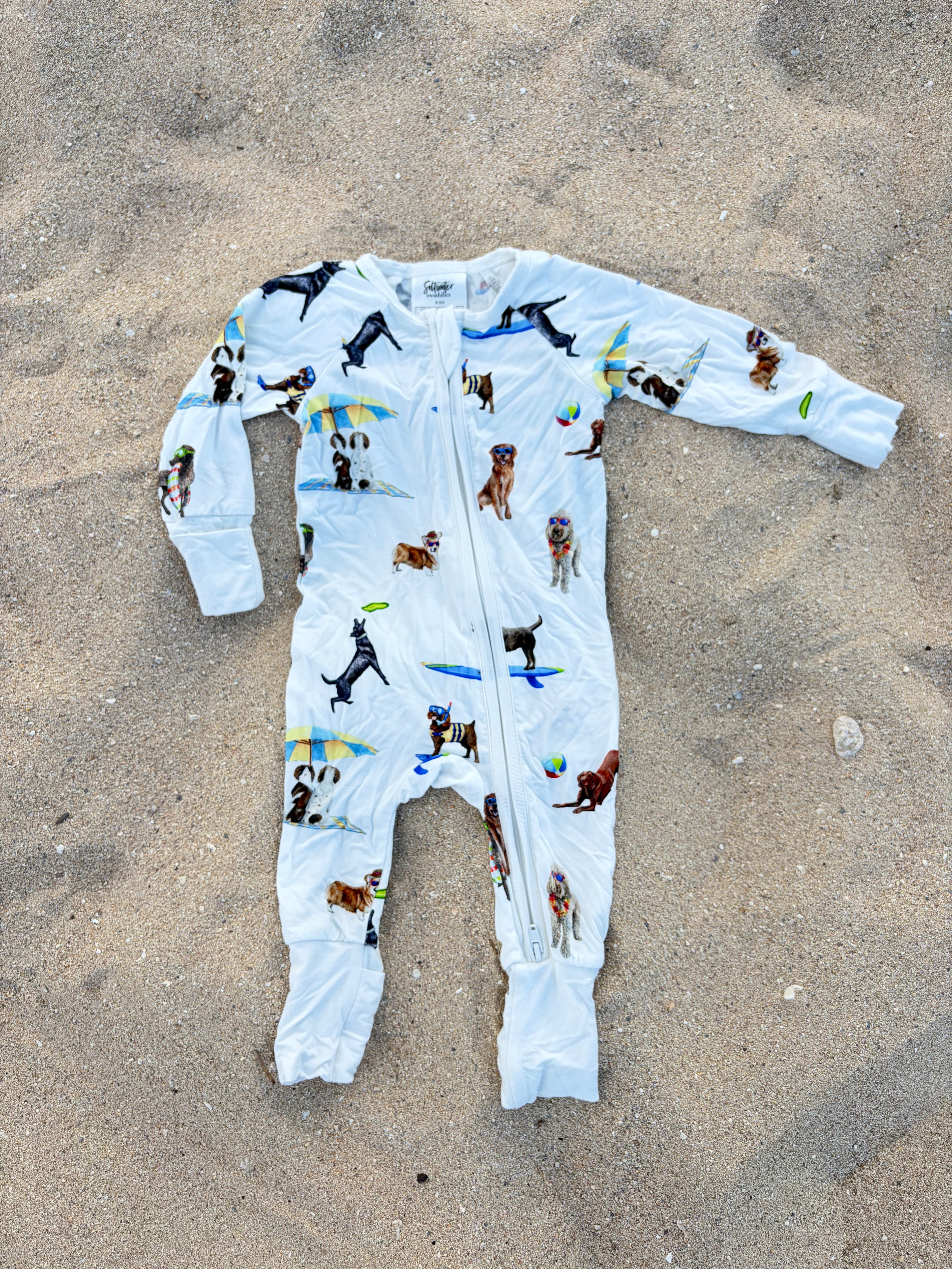 Dog Days of Summer pattern Convertible Zip Footies, made from 100% bamboo and printed on soft white fabric. Displayed flat on the beach sand.