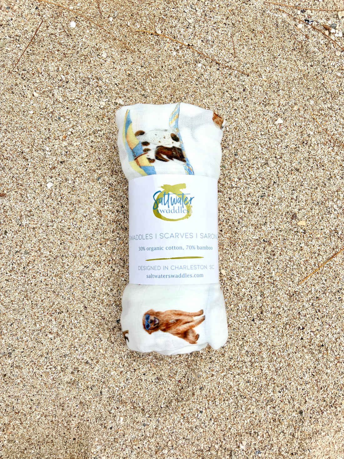 Dog Days of Summer pattern swaddle displayed rolled with the Saltwater Swaddles label on beach sand.