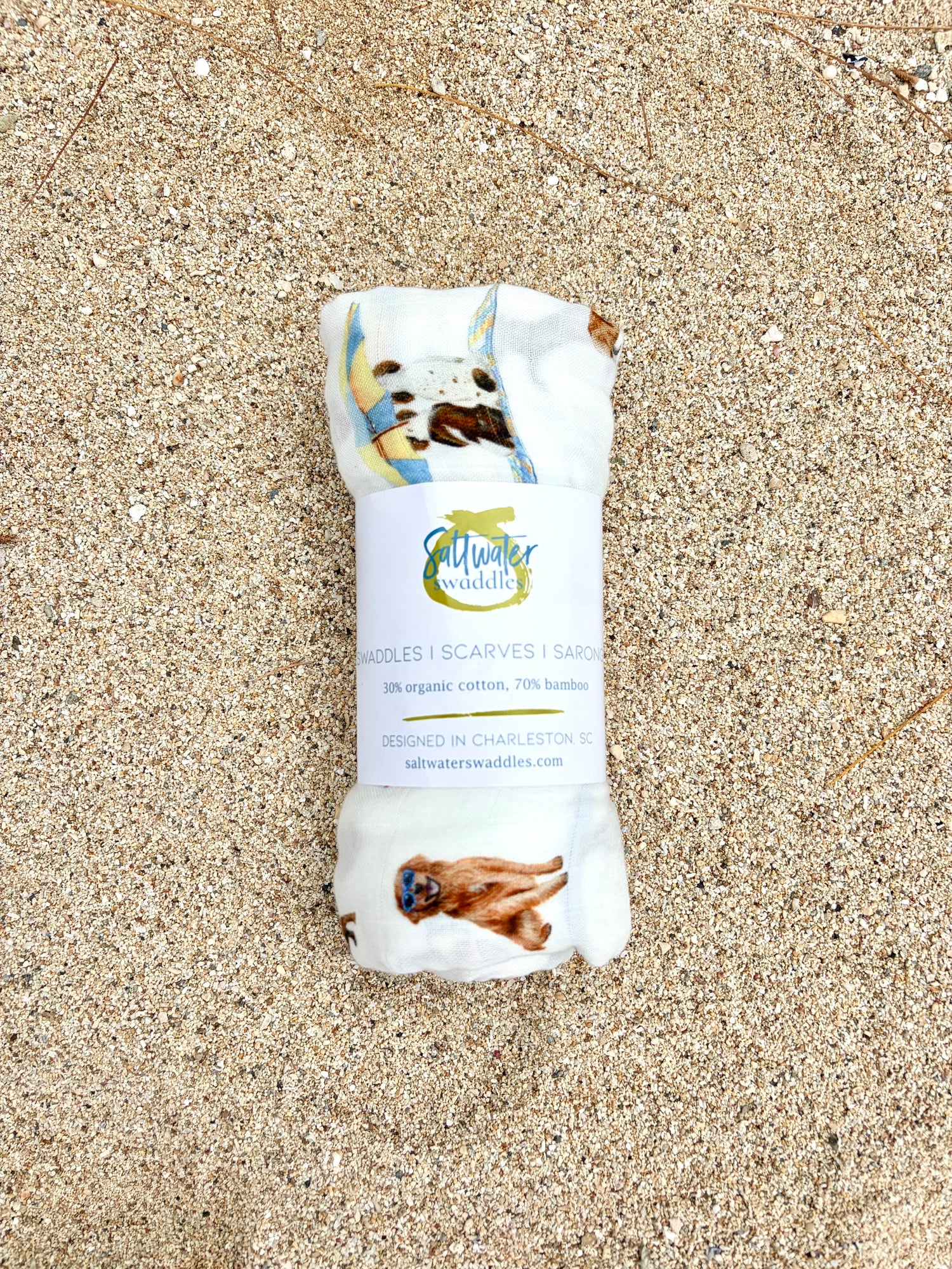 Dog Days of Summer pattern swaddle displayed rolled with the Saltwater Swaddles label on beach sand.