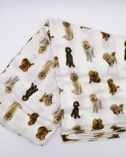 Flat-lay of a folded muslin baby swaddle blanket covered in realistic sitting and standing goldendoodle dog pattern.