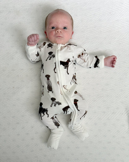 A baby lying, wearing a bamboo zip footie with a pattern of German Shorthaired Pointers.