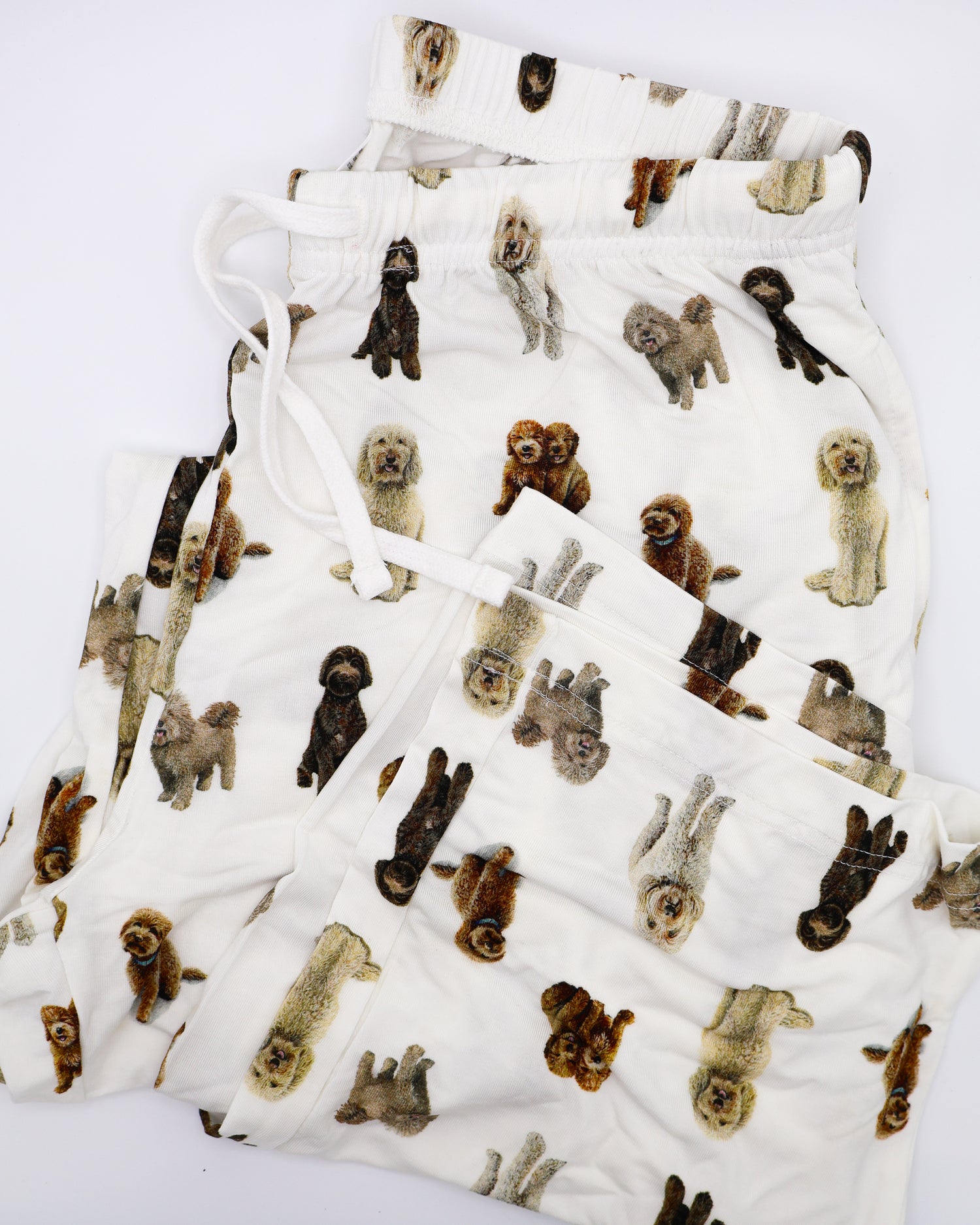 Folded soft white adult pajama pants featuring an all-over realistic goldendoodle pattern with an elastic waistband and white drawstring tie.