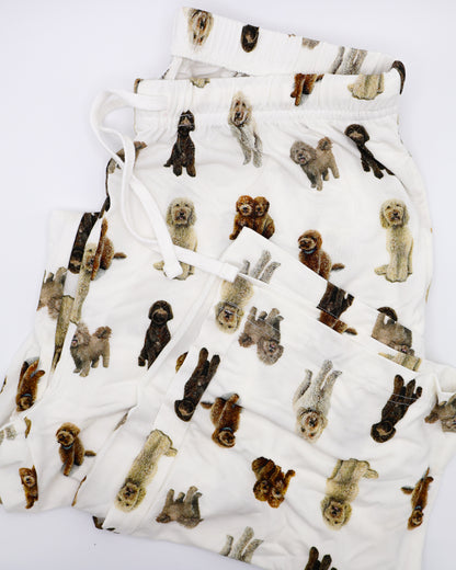 Folded soft white adult pajama pants featuring an all-over realistic goldendoodle pattern with an elastic waistband and white drawstring tie.