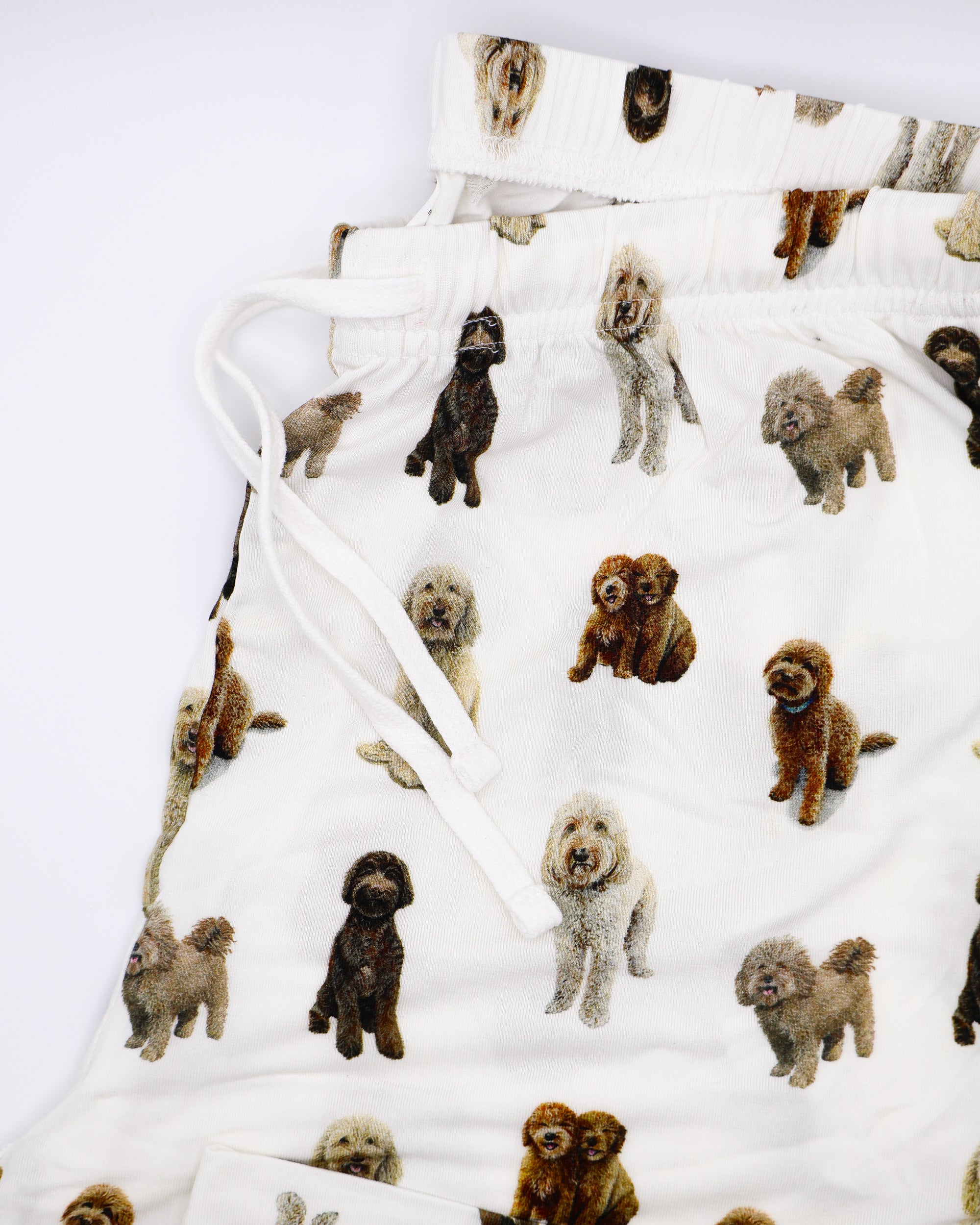 Folded soft white adult pajama pants featuring an all-over realistic goldendoodle pattern with an elastic waistband and white drawstring tie.