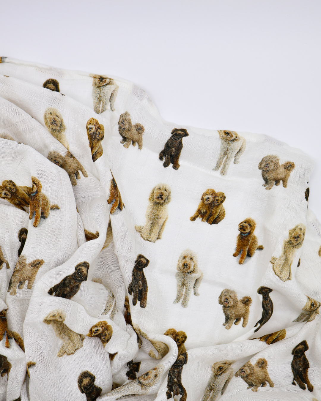 Flat-lay of an unfolded muslin baby swaddle blanket covered in realistic sitting and standing goldendoodle dog pattern.