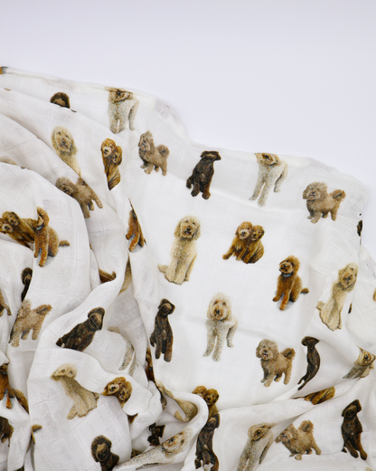 Flat-lay of an unfolded muslin baby swaddle blanket covered in realistic sitting and standing goldendoodle dog pattern.