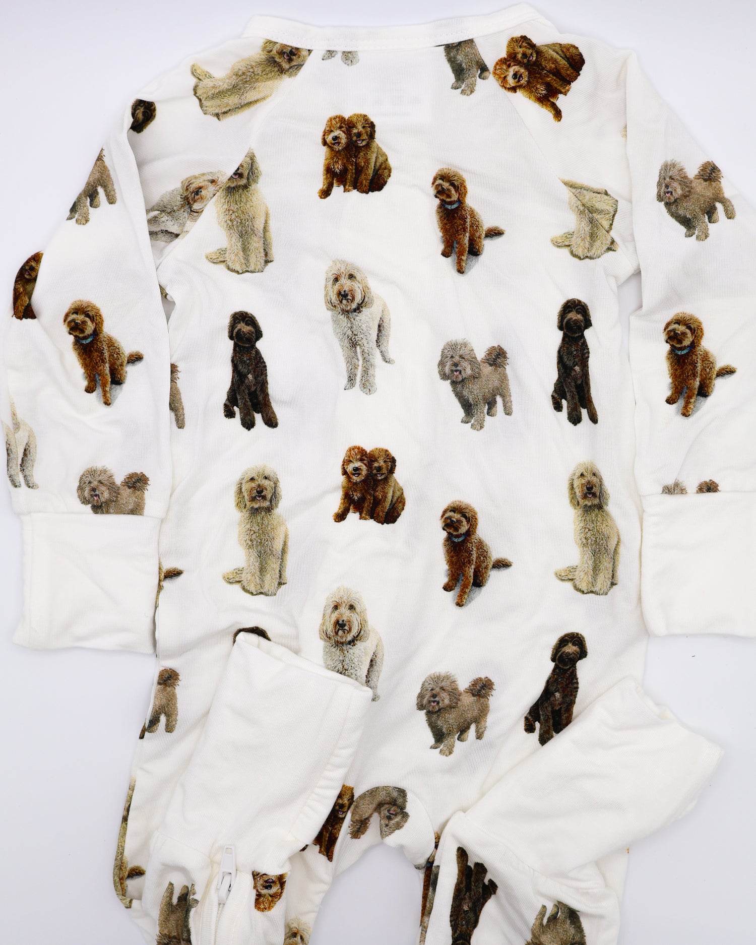 Flat-lay view of a long-sleeve goldendoodle pattern convertible zip footies, a baby romper with two-way zipper and convertible fold-over feet.