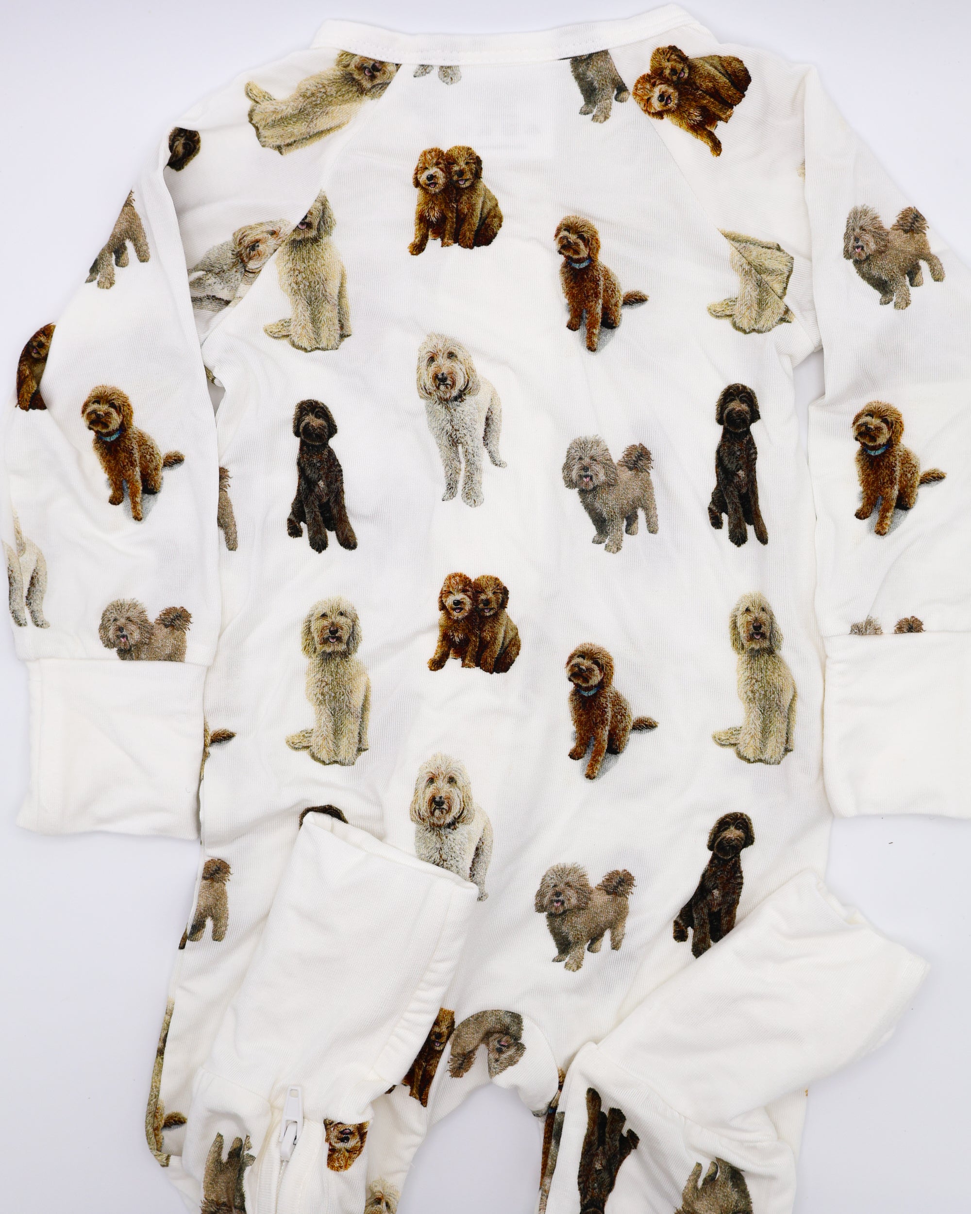 Flat-lay view of a long-sleeve goldendoodle pattern convertible zip footies, a baby romper with two-way zipper and convertible fold-over feet.