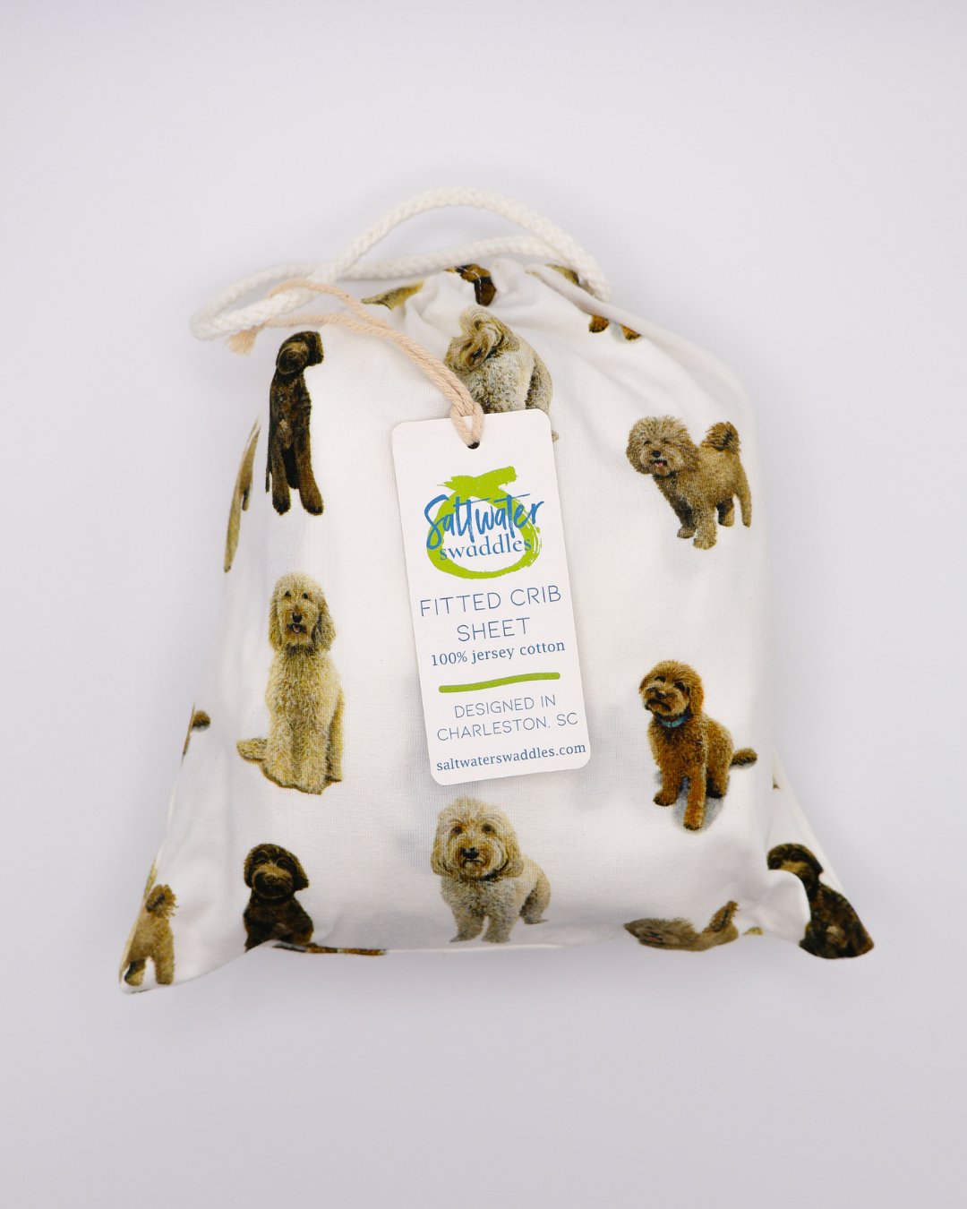 Fitted cotton crib sheet featuring an all-over goldendoodle dog pattern in a crib sheet bag on a crisp white background.