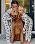 Two young children playing together outdoors, wearing matching two-piece white pajama sets patterned with hand-painted goldendoodle dogs and with their goldendoodle dog.