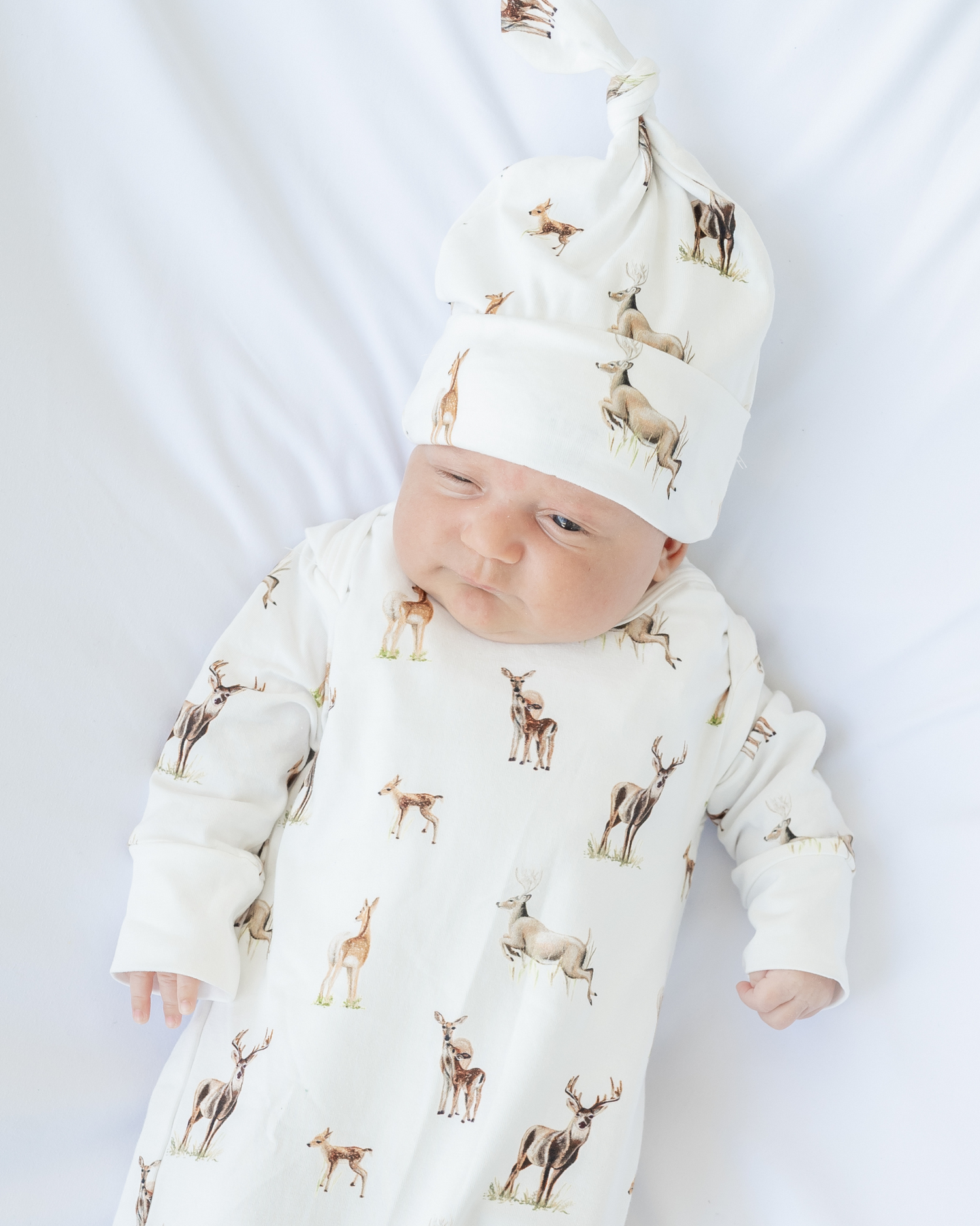 Little Fawn Big Yawn Deer newborn gown and matching hat, made from soft white cotton jersey with bottom flaps for knotting, cozy and perfect for your hospital bag. Worn by a baby.