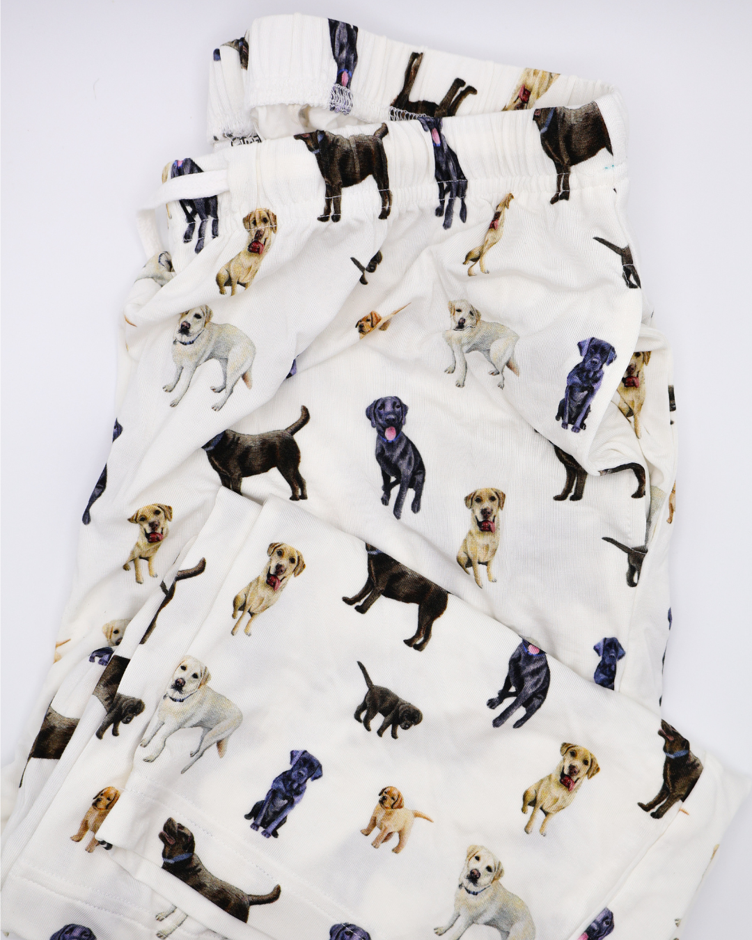 White adult pants with an all-over pattern of black, chocolate, and yellow labs, shown folded on a white background.