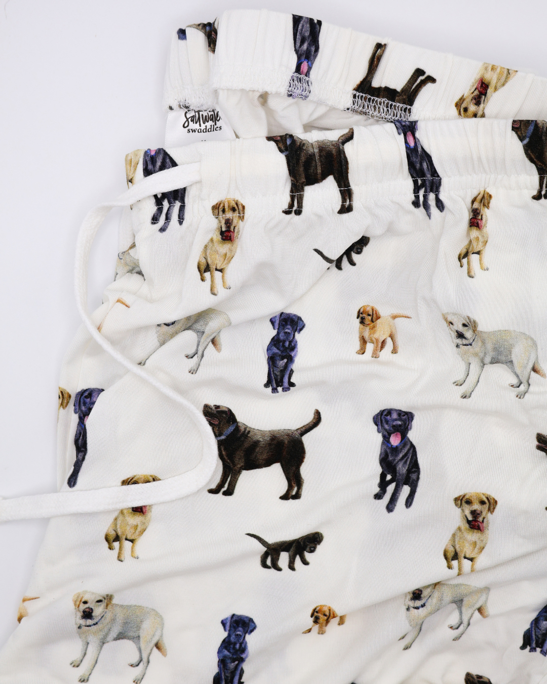 Close up of a white adult pants with an all-over pattern of black, chocolate, and yellow labs, shown folded on a white background.
