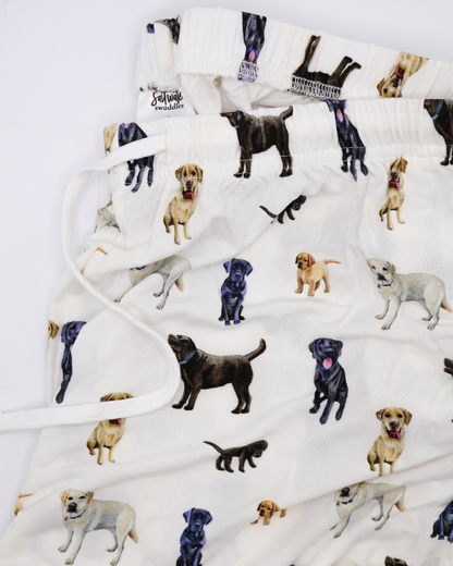 Close up of a white adult pants with an all-over pattern of black, chocolate, and yellow labs, shown folded on a white background.