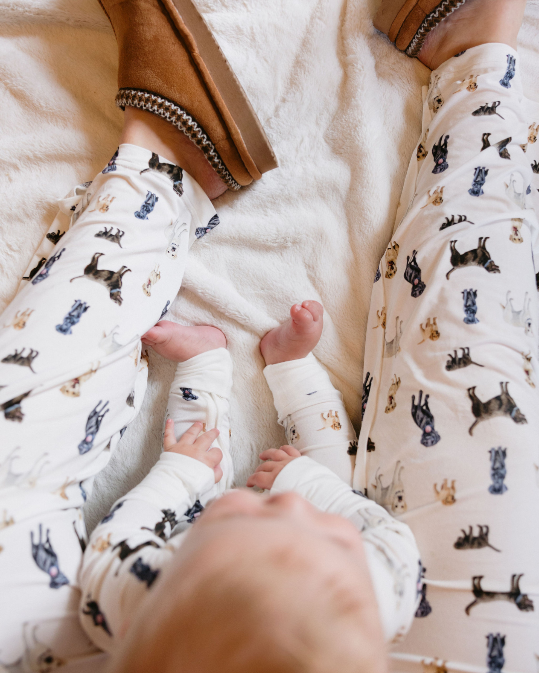 Furmom wearing Loyal Labs Adult Pajama Pants featuring an adorable print of chocolate, yellow, and black Labrador retrievers while enjoying a cozy moment indoors with her baby.