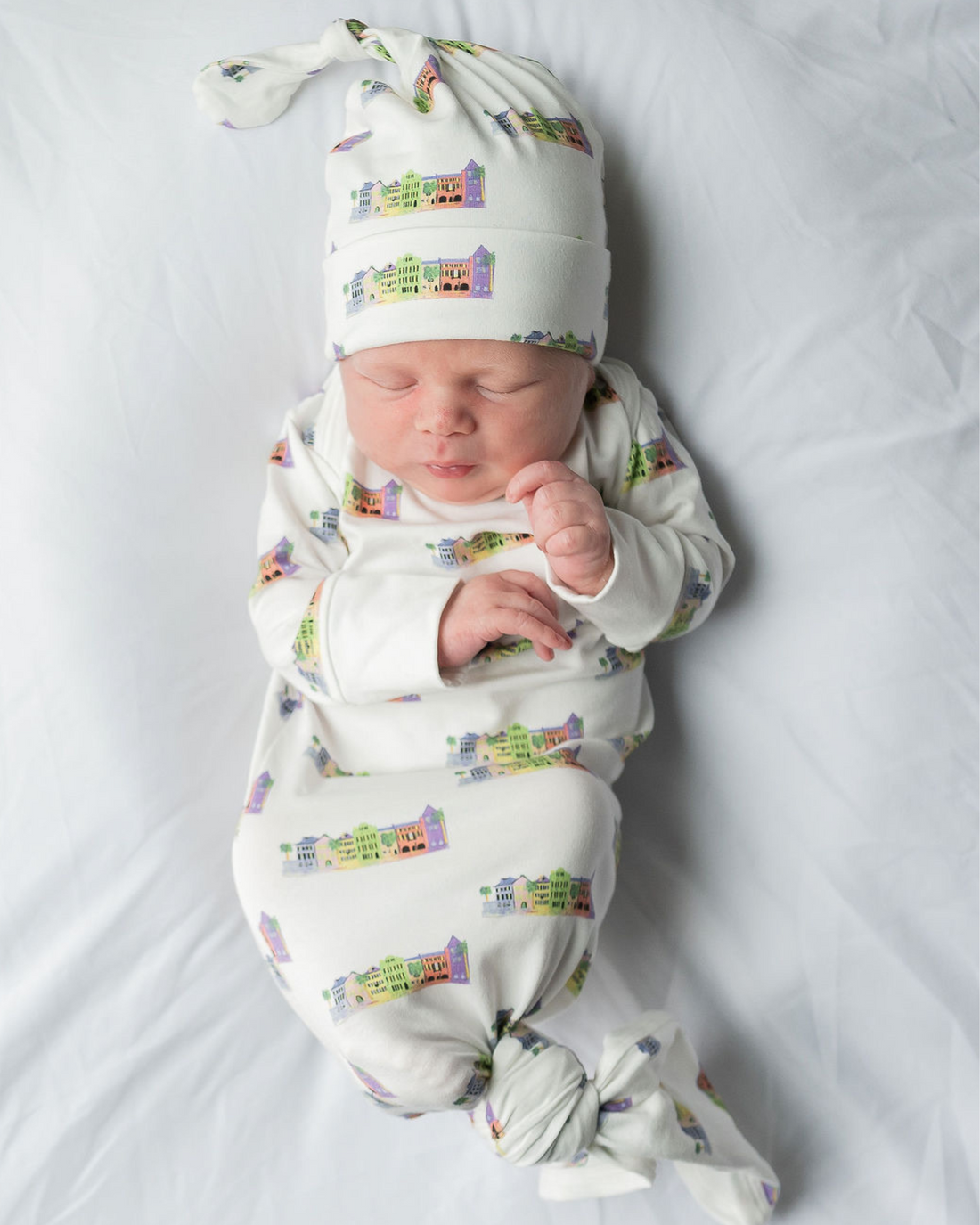 Baby wrapped in cozy Rainbow Row-themed gown and hat, capturing early memories