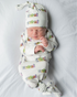 Baby wrapped in cozy Rainbow Row-themed gown and hat, capturing early memories
