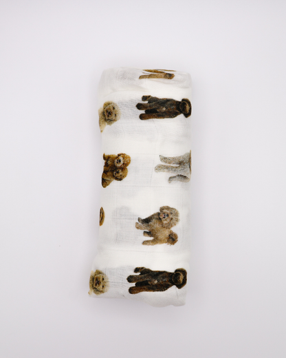 Flat-lay of a rolled muslin baby swaddle blanket covered in realistic sitting and standing goldendoodle dog pattern.