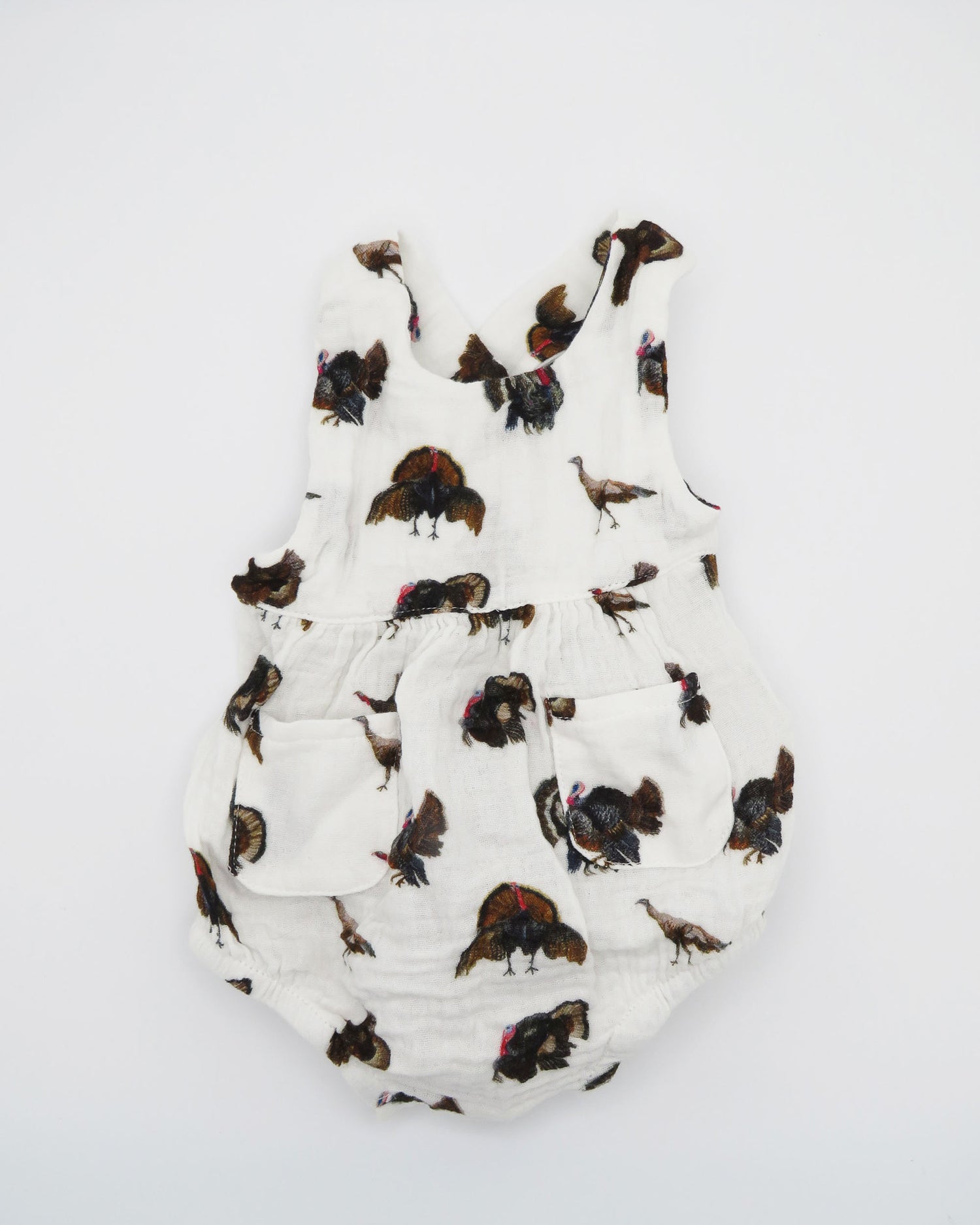 Turkey Trot baby sunsuit in soft white fabric with a playful turkey print, lightweight and comfortable for all-day wear. Perfect for keeping babies cozy indoors or outdoors, ideal for festive fall or Thanksgiving outfits. Displayed flat on white background.