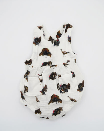 Turkey Trot baby sunsuit in soft white fabric with a playful turkey print, lightweight and comfortable for all-day wear. Perfect for keeping babies cozy indoors or outdoors, ideal for festive fall or Thanksgiving outfits. Displayed flat on white background.