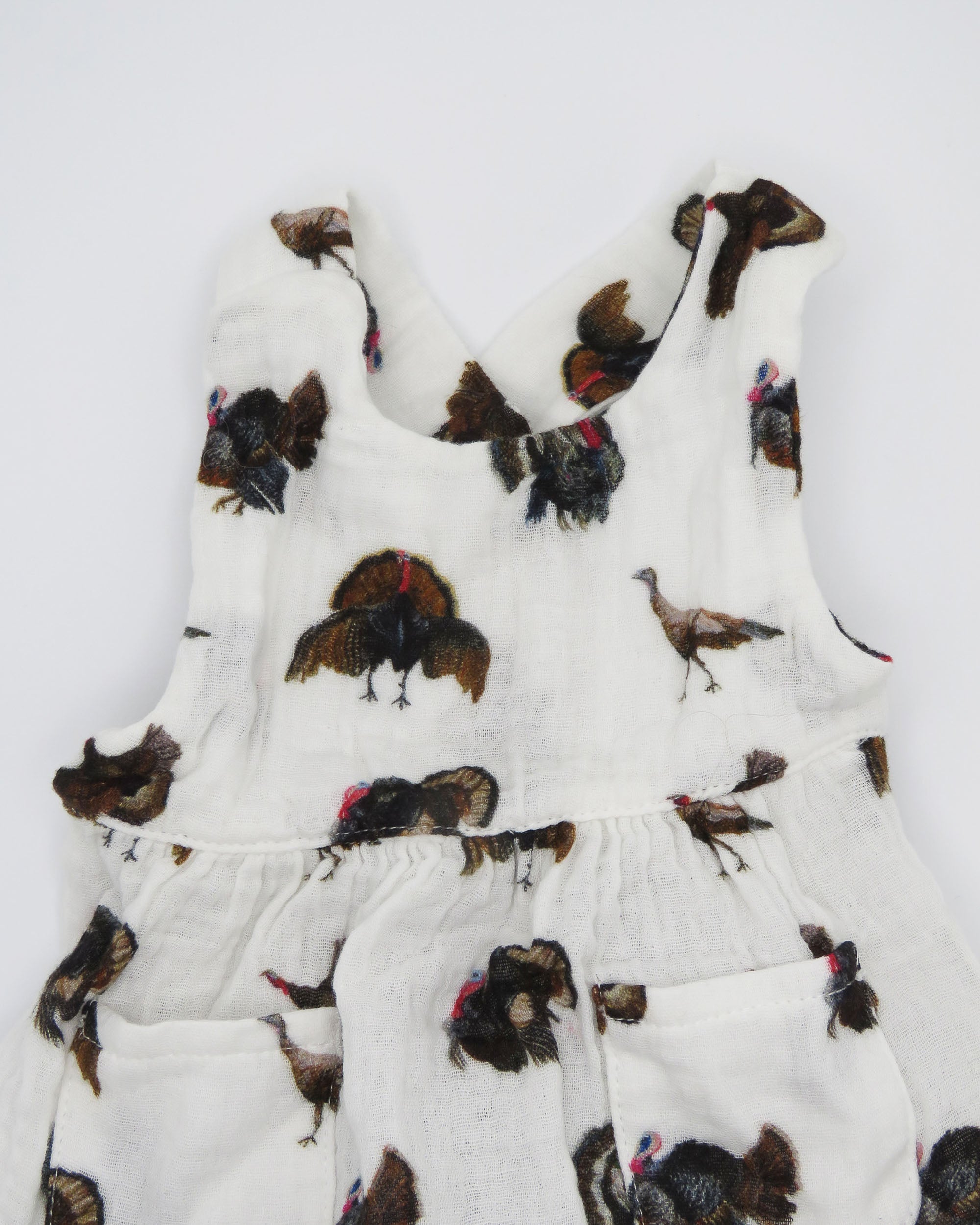 Turkey Trot baby sunsuit in soft white fabric with a playful turkey print, lightweight and comfortable for all-day wear. Perfect for keeping babies cozy indoors or outdoors, ideal for festive fall or Thanksgiving outfits. Displayed flat on white background.