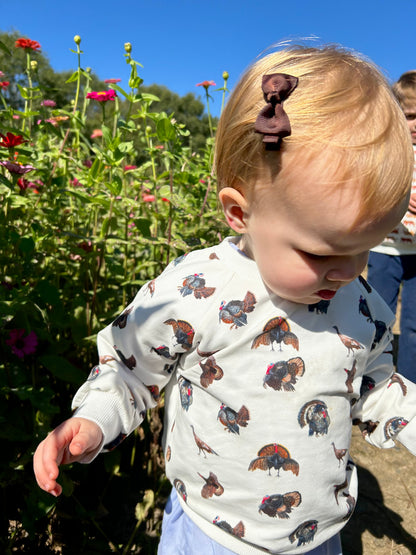 Turkey Trot kids’ drop sleeve sweatshirt in soft white fabric with a playful turkey print, cozy and comfortable for indoors or outdoors. Shown worn by a little girl playing outside.