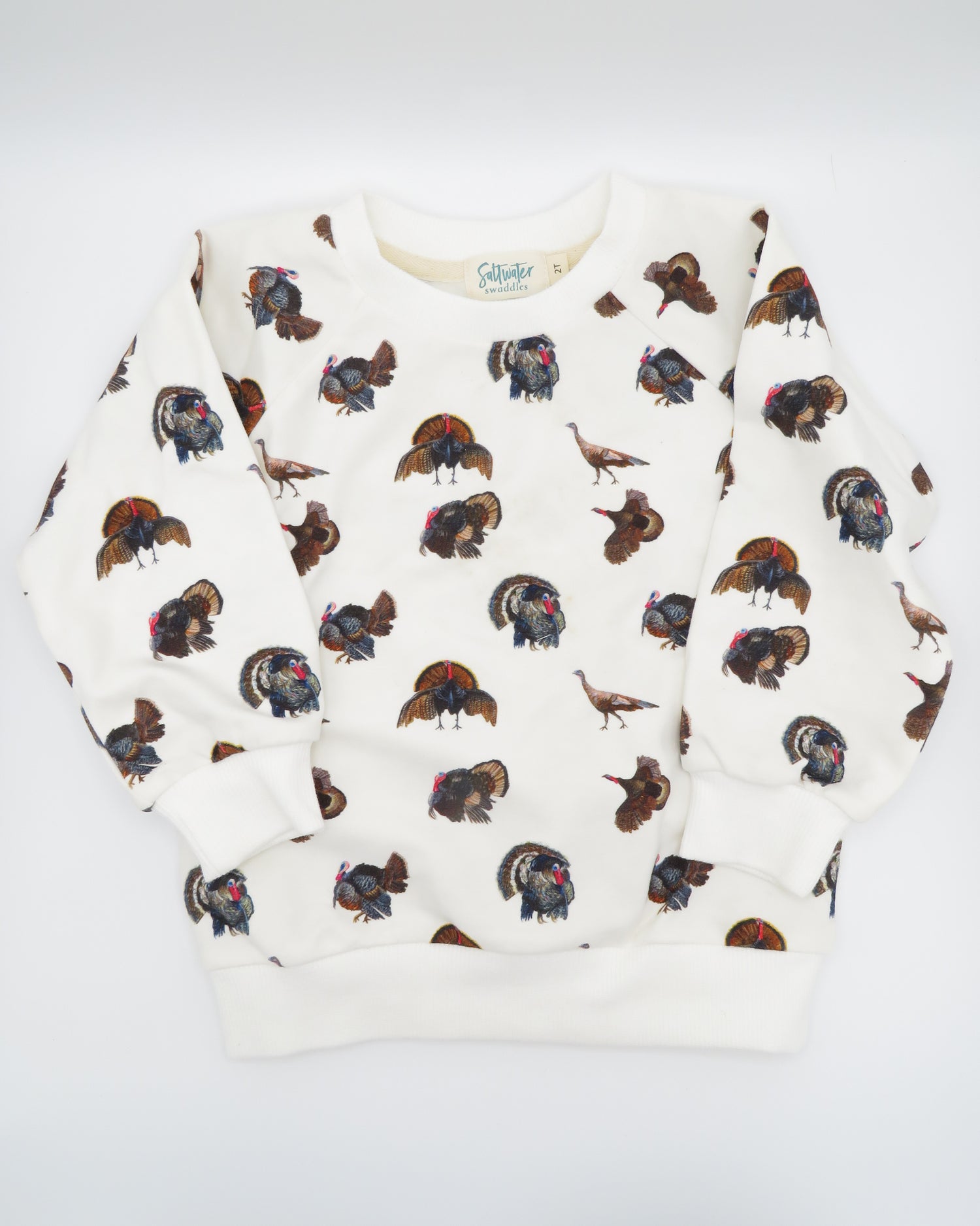 Turkey Trot kids’ drop sleeve sweatshirt in soft white fabric with a playful turkey print, cozy and comfortable for indoors or outdoors. Displayed flat on white background.